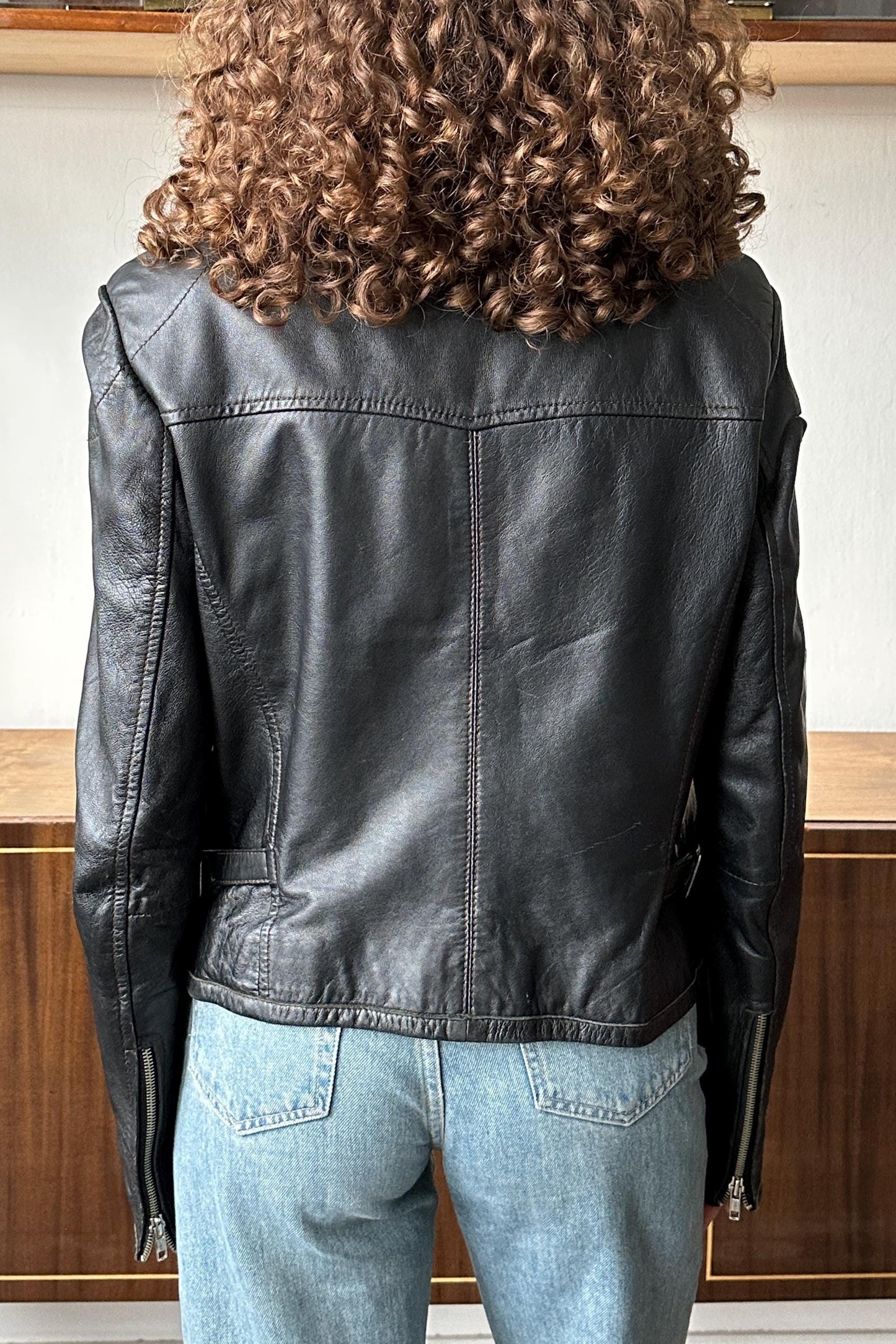 the back of a person wearing a black leather jacket and blue jeans.