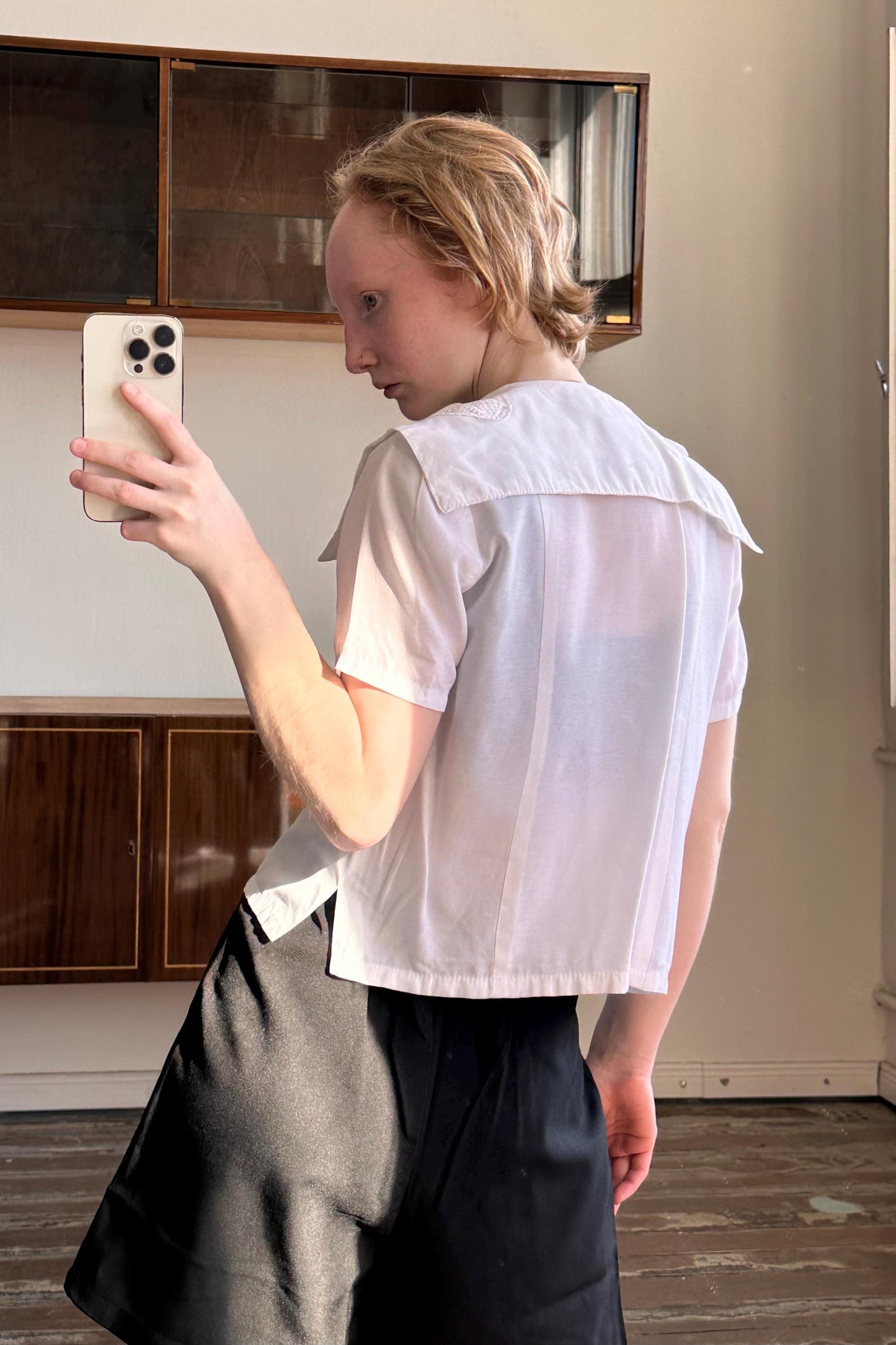 A person is taking a selfie with a smartphone in a room with wooden cabinets in the background.