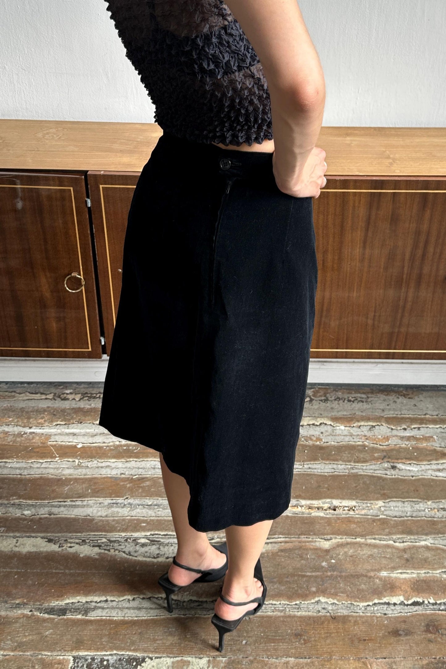 A person wearing a black skirt and top stands in front of a wooden cabinet.