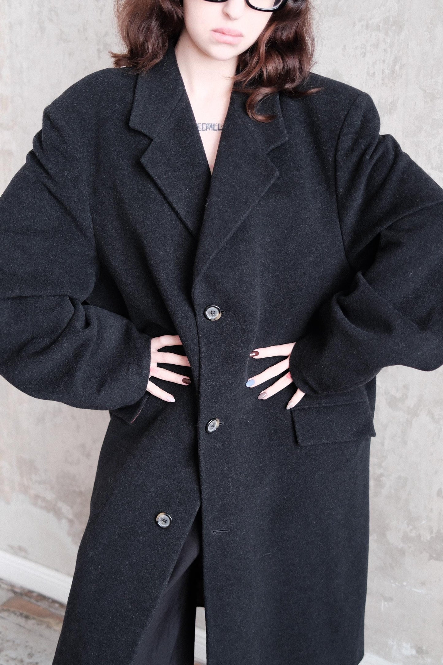 A person wearing a black coat is standing on a concrete floor.