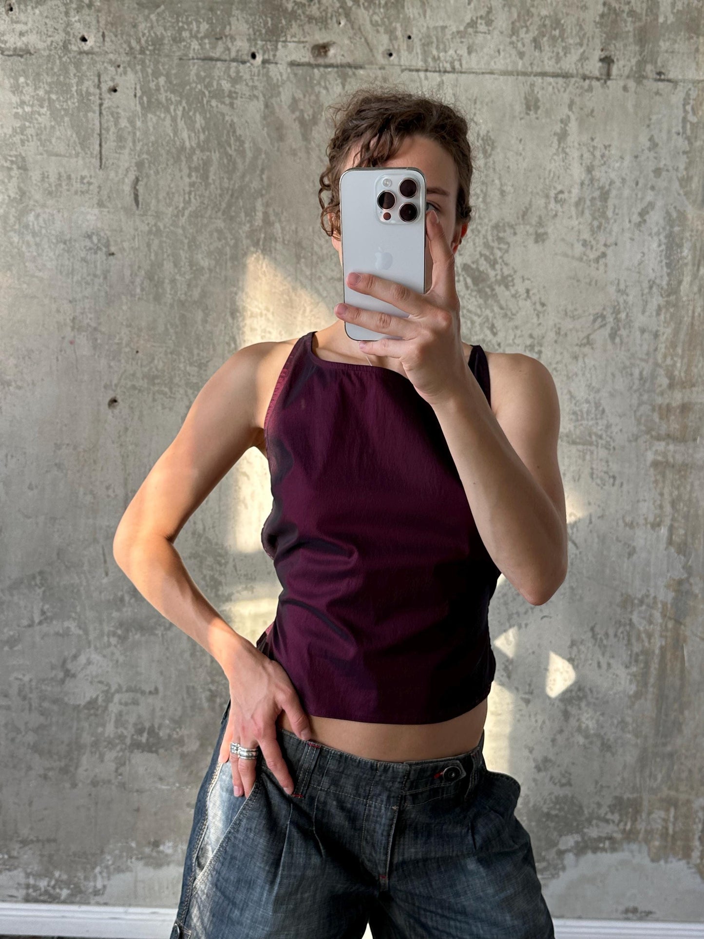 A person is taking a selfie with a smartphone, holding it up to their face against a concrete wall background.