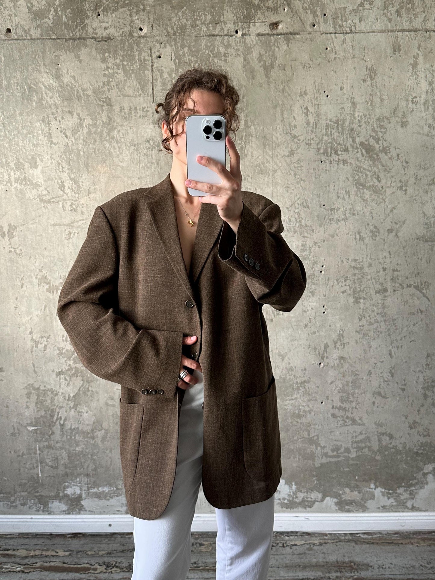 A person is taking a selfie with a smartphone, holding it up to their face against a concrete wall.