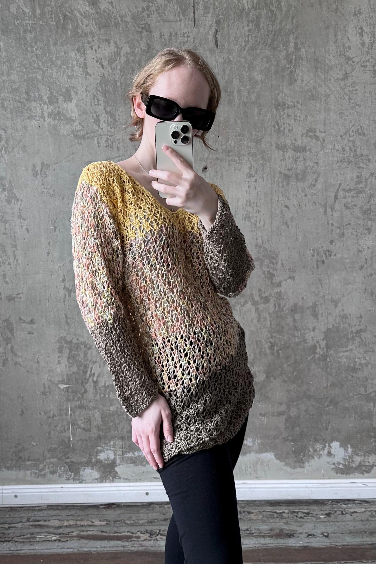 A person is taking a selfie with a smartphone, wearing a colorful, patterned sweater and sunglasses.