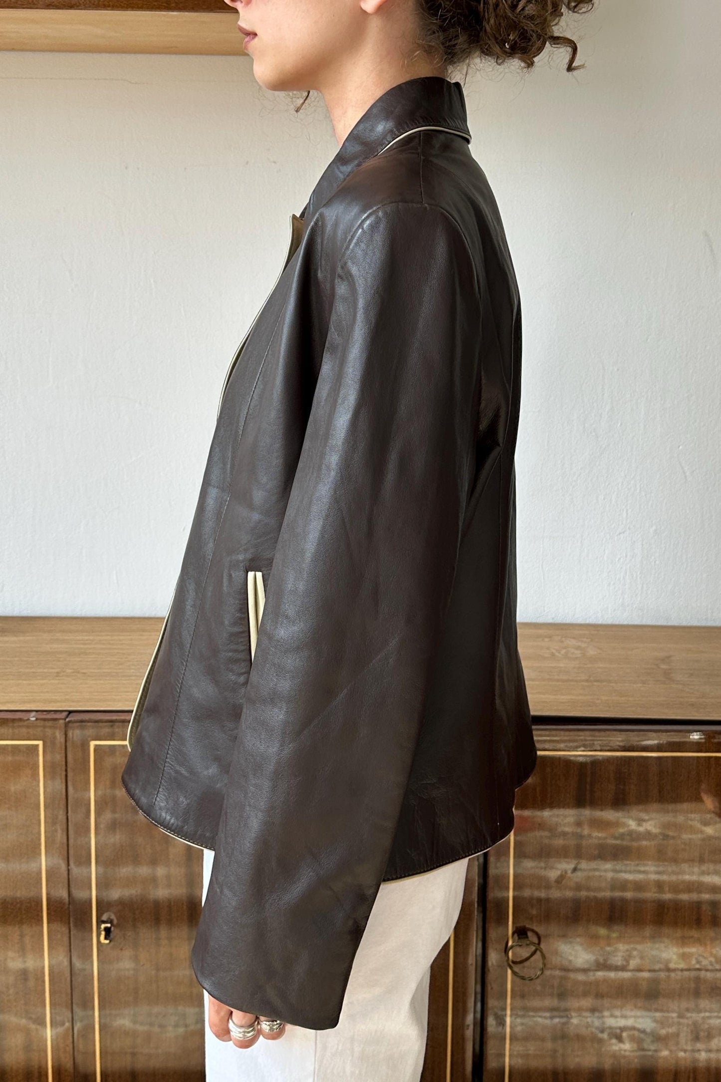 A woman wearing a black leather jacket stands in front of a wooden cabinet.