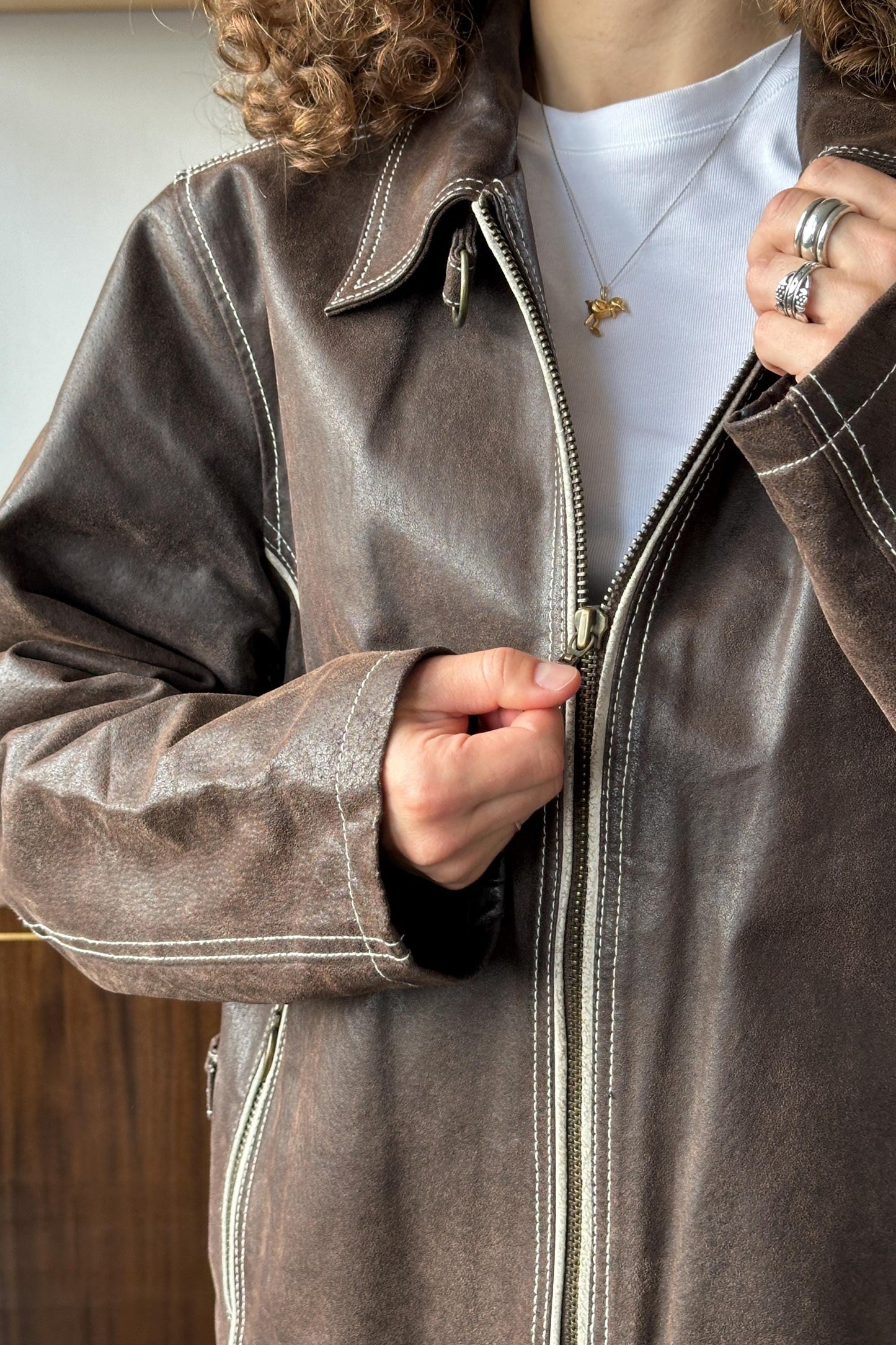 A close-up of a person wearing a brown leather jacket with a zipper, and a white t-shirt underneath.