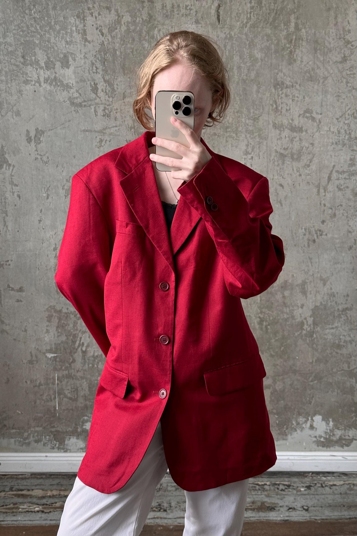 A person wearing a red blazer is taking a selfie with a smartphone.