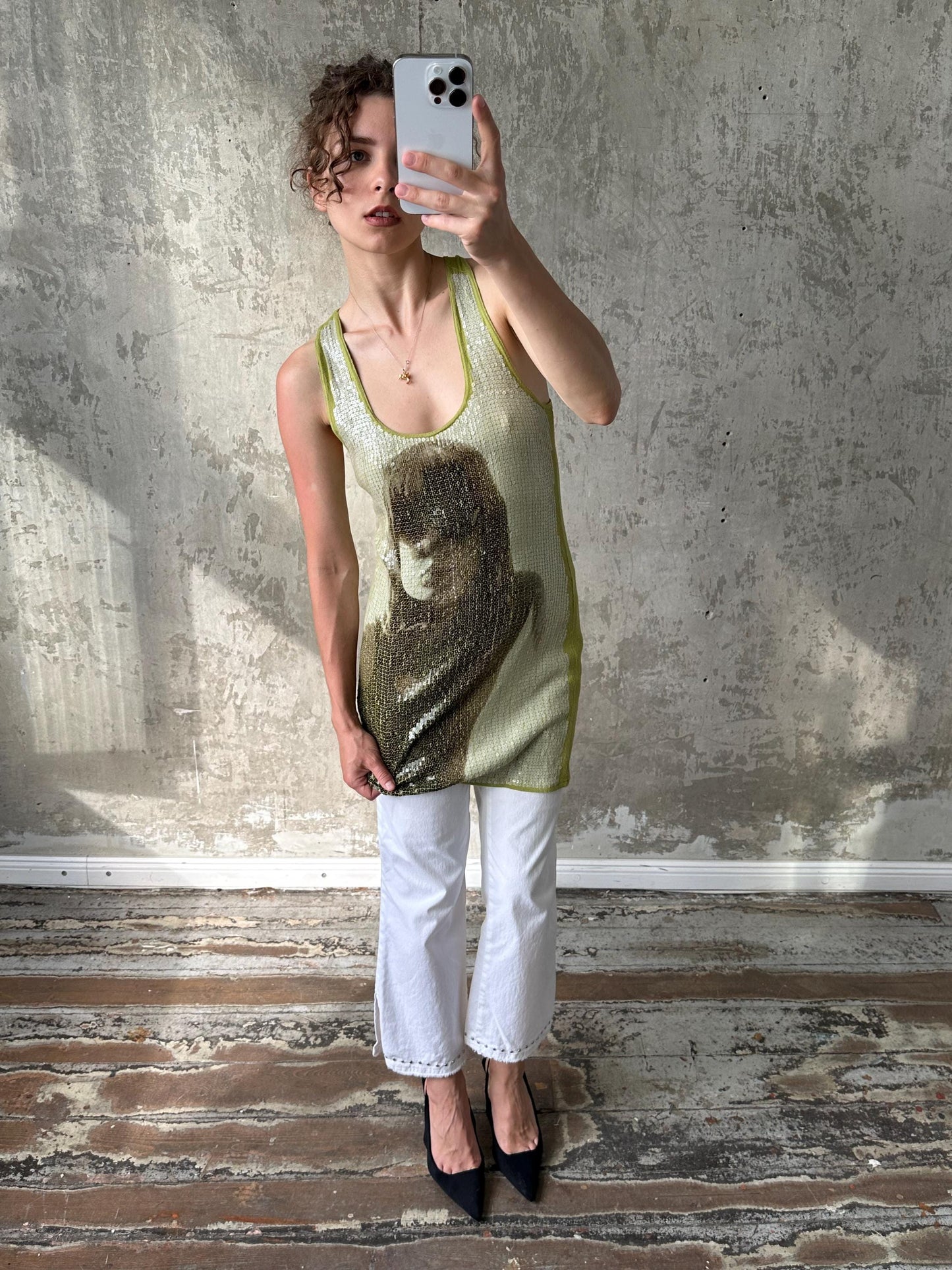 A woman is taking a selfie with a smartphone, holding the device up to her face against a concrete wall.