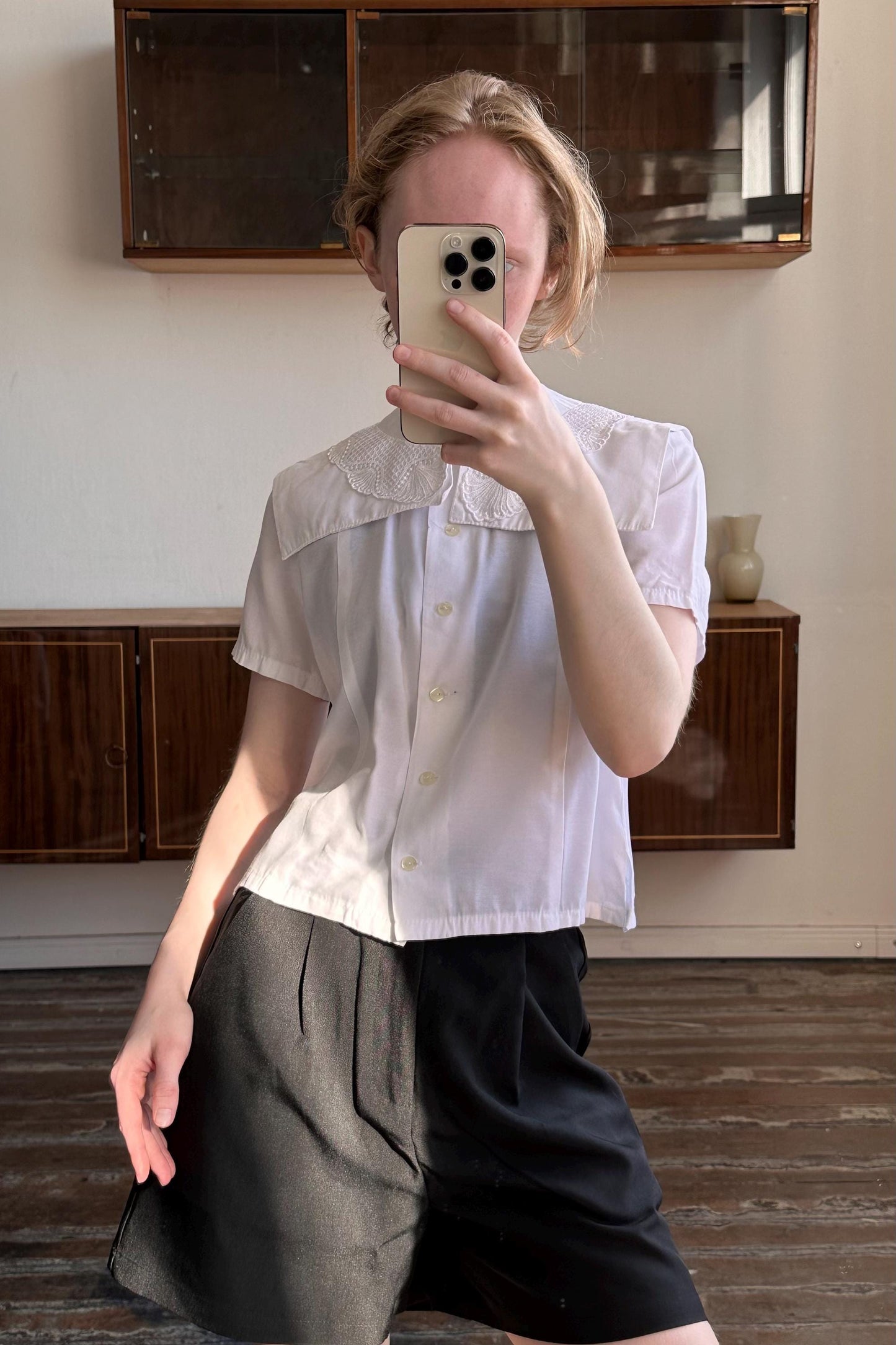 A person is taking a selfie with a white shirt and black skirt, holding a smartphone in front of their face.