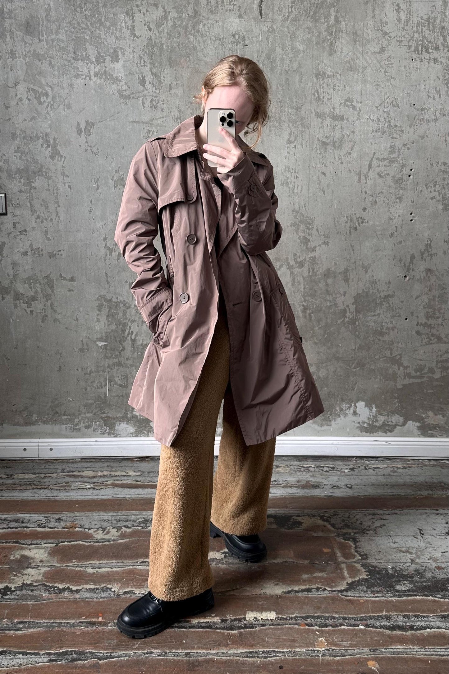 A person is taking a selfie with a smartphone, standing in front of a concrete wall.
