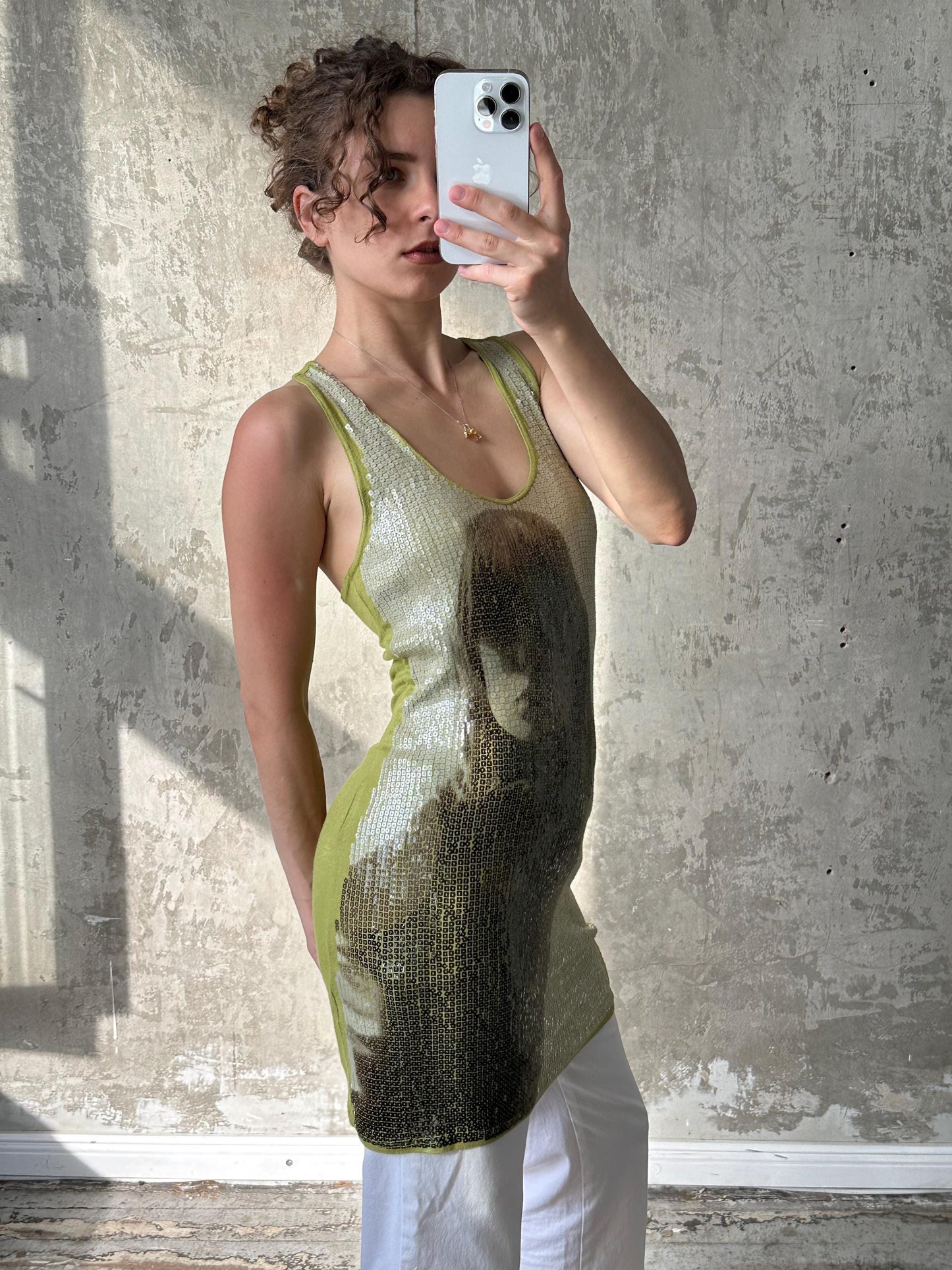 A woman is taking a selfie with a smartphone, wearing a sleeveless dress with a patterned design.