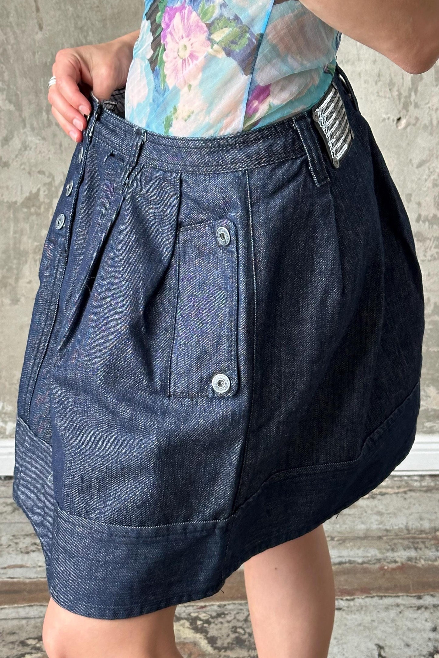 A person wearing a blue denim skirt with a floral pattern and a silver belt buckle.