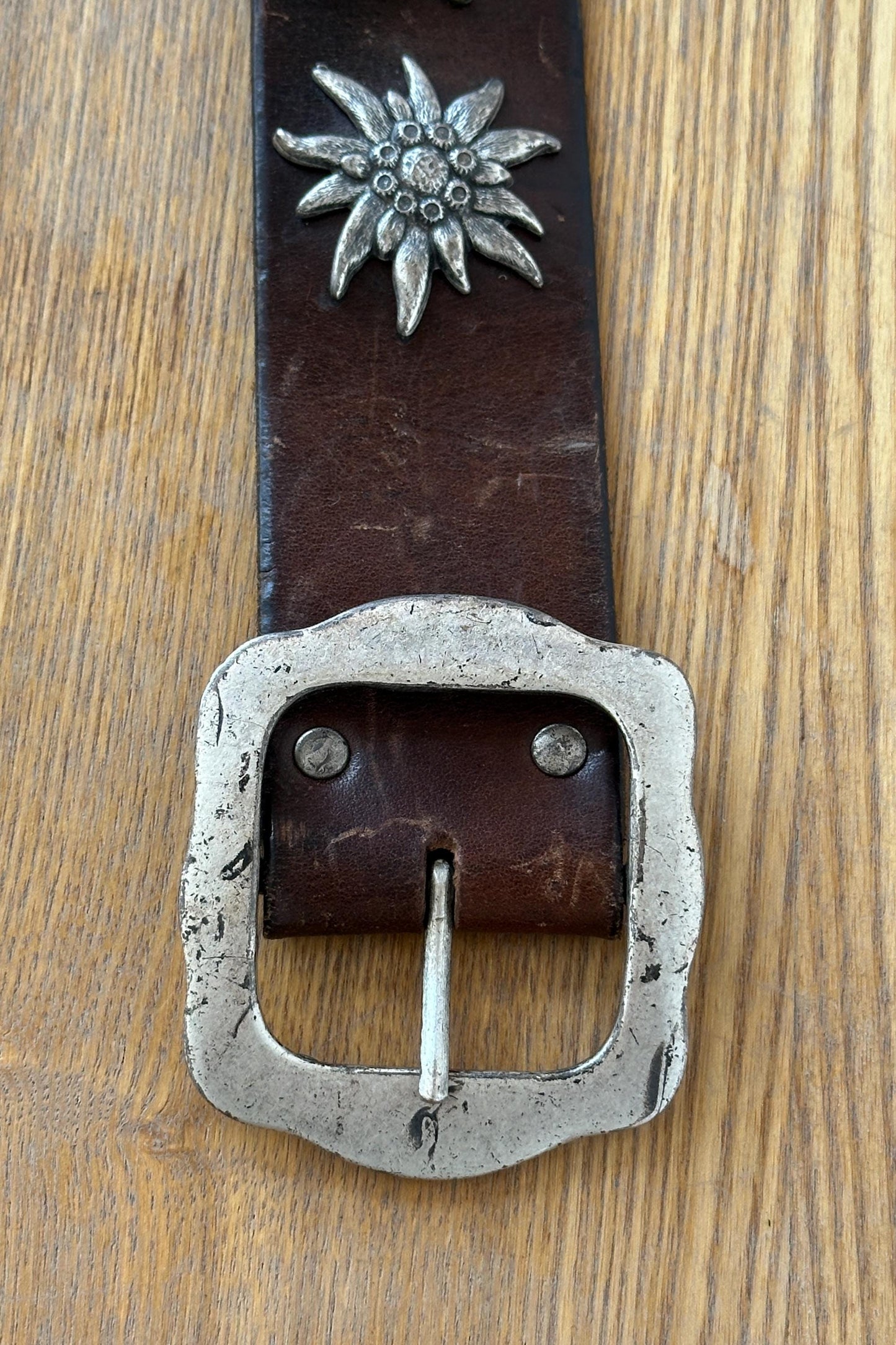 A close-up image of a leather belt with a metal buckle, resting on a wooden surface.