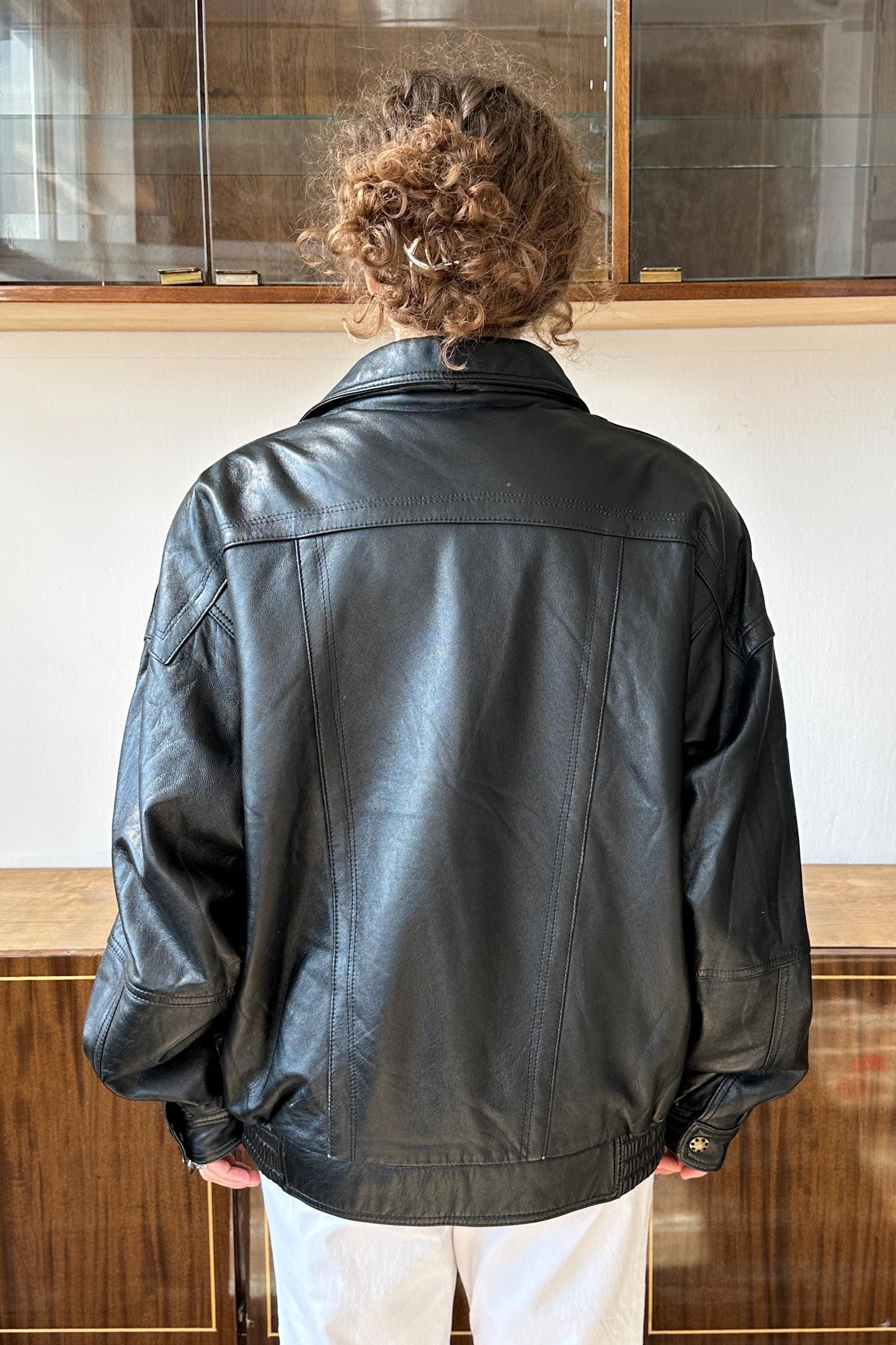 A person wearing a black leather jacket stands in front of a glass display case.