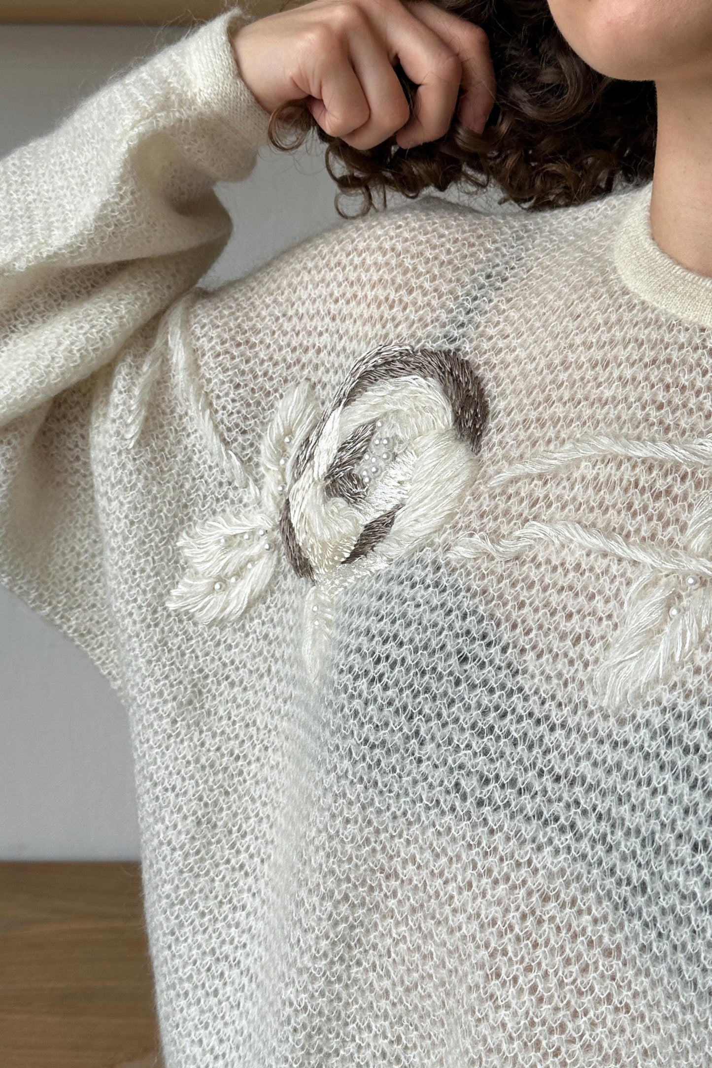 A close-up view of a person's arm wearing a white knitted sweater with a floral embroidered design.