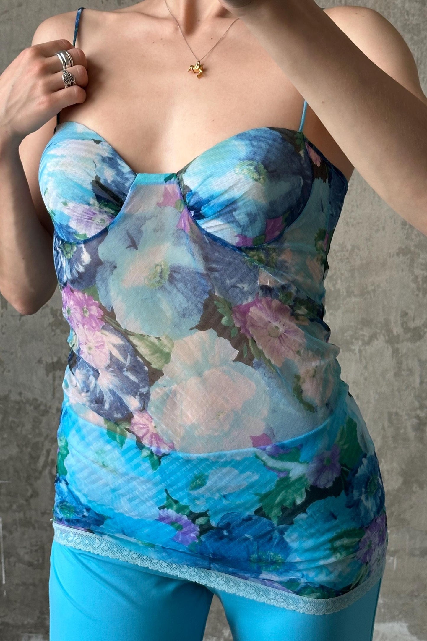 A woman wearing a blue floral print top and matching blue pants, posing with her hands on her chest.