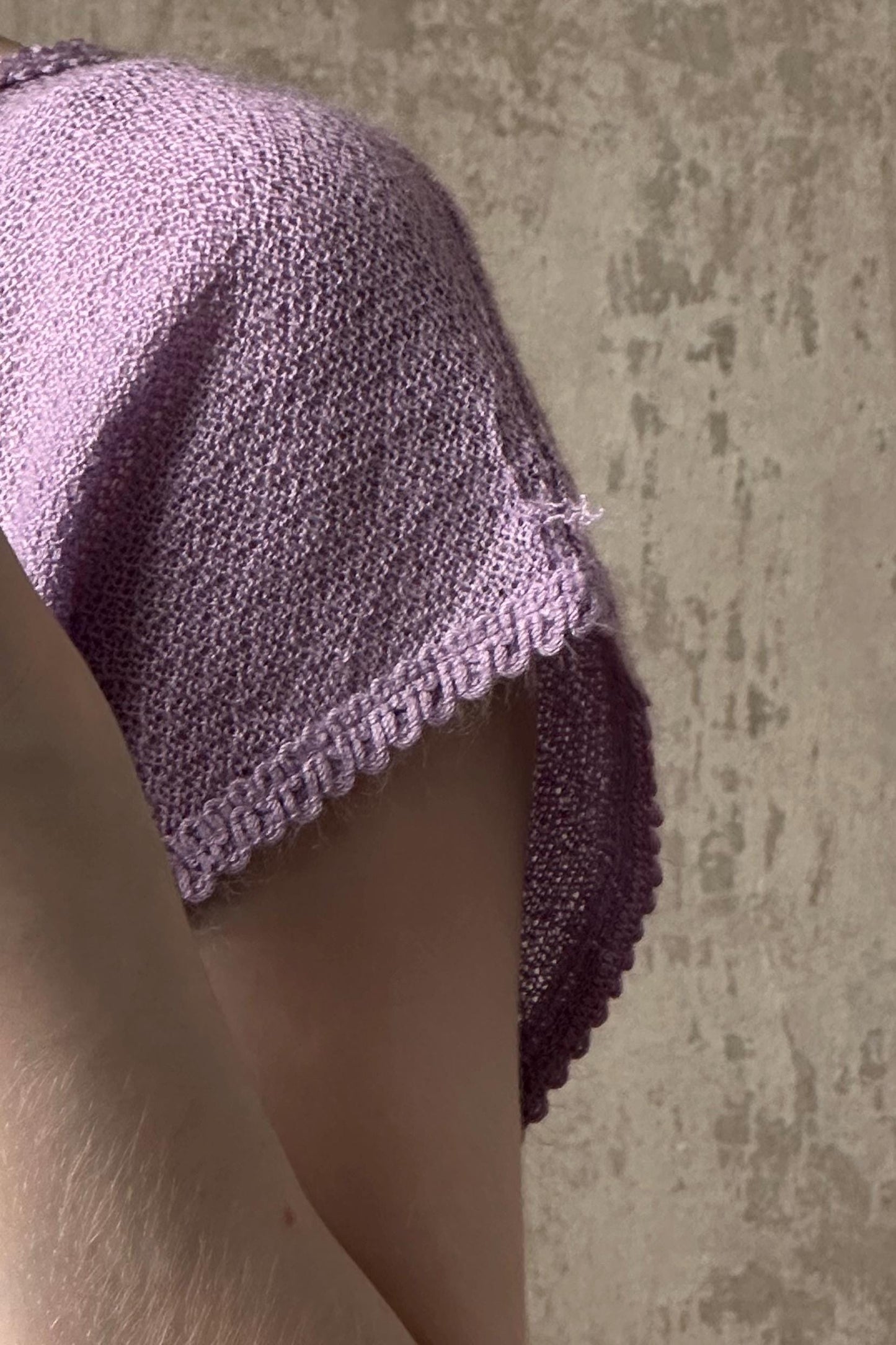 A close-up view of a purple knitted garment, possibly a sweater or a shawl, with a scalloped edge and a small tear visible.