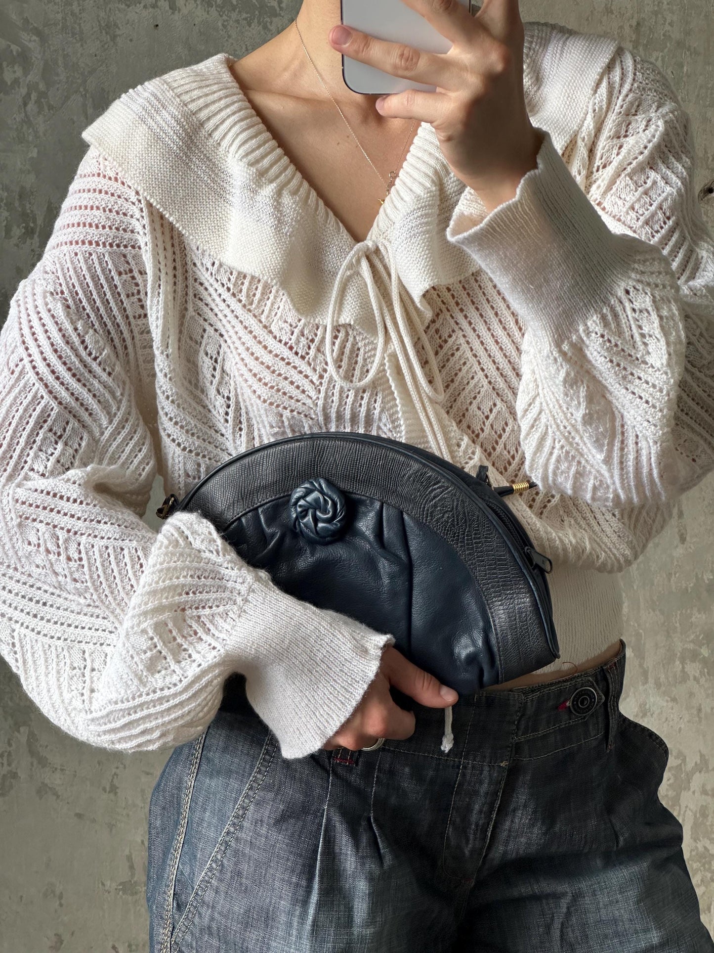 A person is holding a black purse with a floral design, wearing a white sweater and blue jeans.