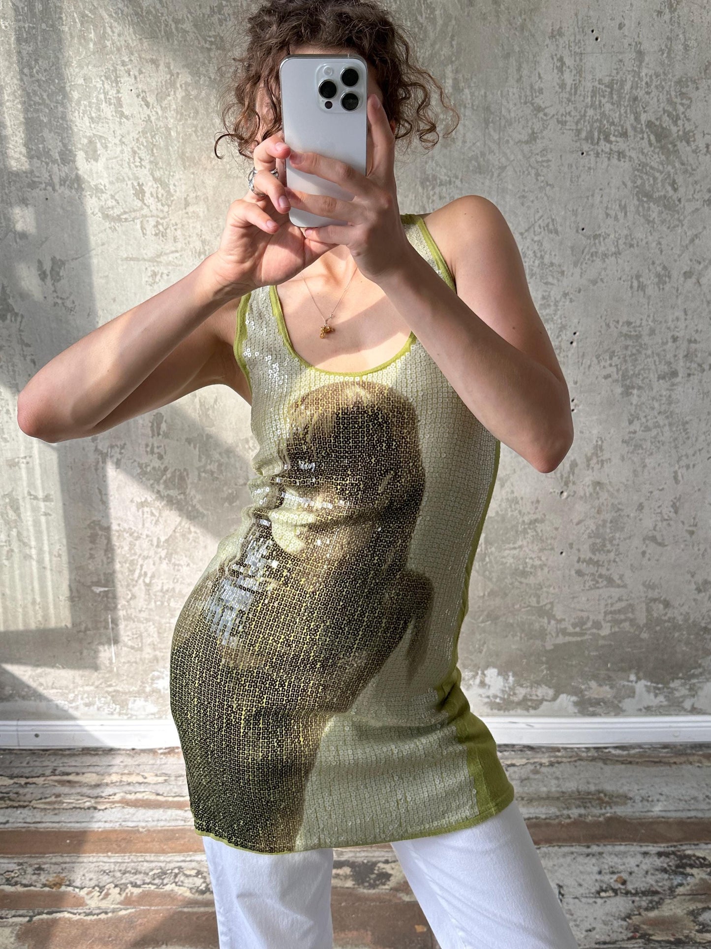 A person is taking a selfie with a smartphone, wearing a sleeveless top with a graphic design on it.