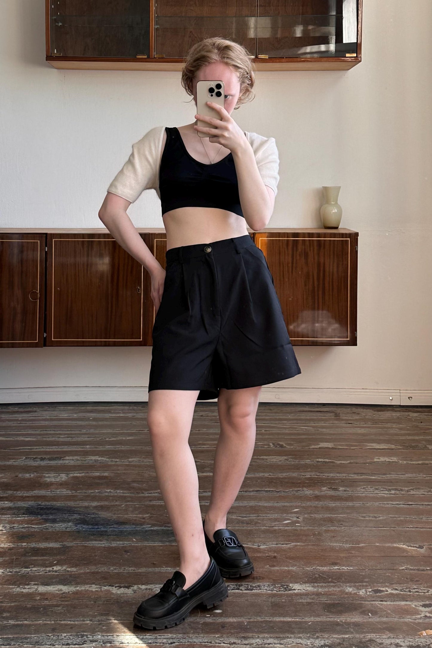 A person is taking a selfie with a smartphone in a room with wooden floors and wooden cabinets.
