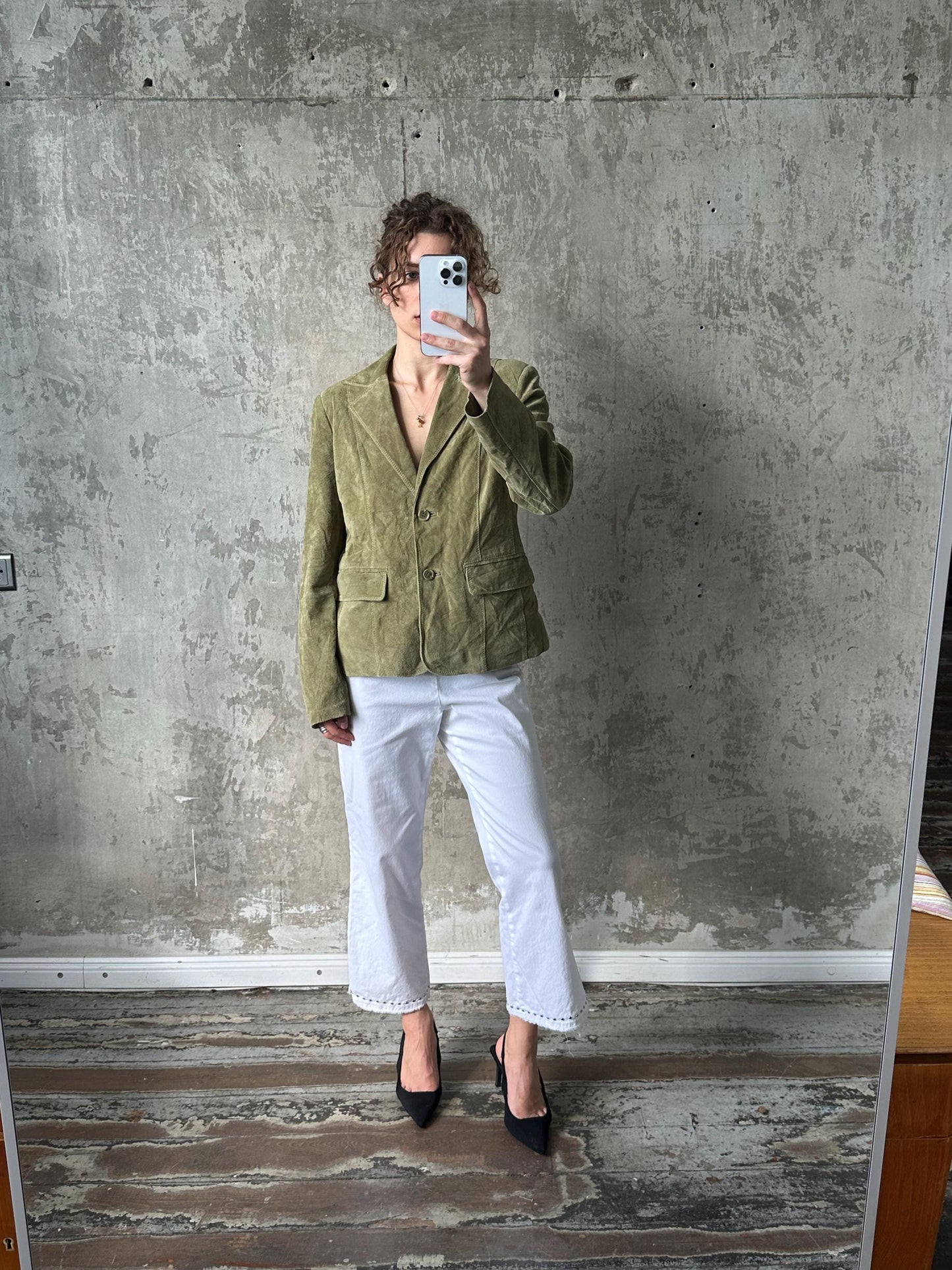A person is taking a selfie in front of a concrete wall, holding a phone up to their face.