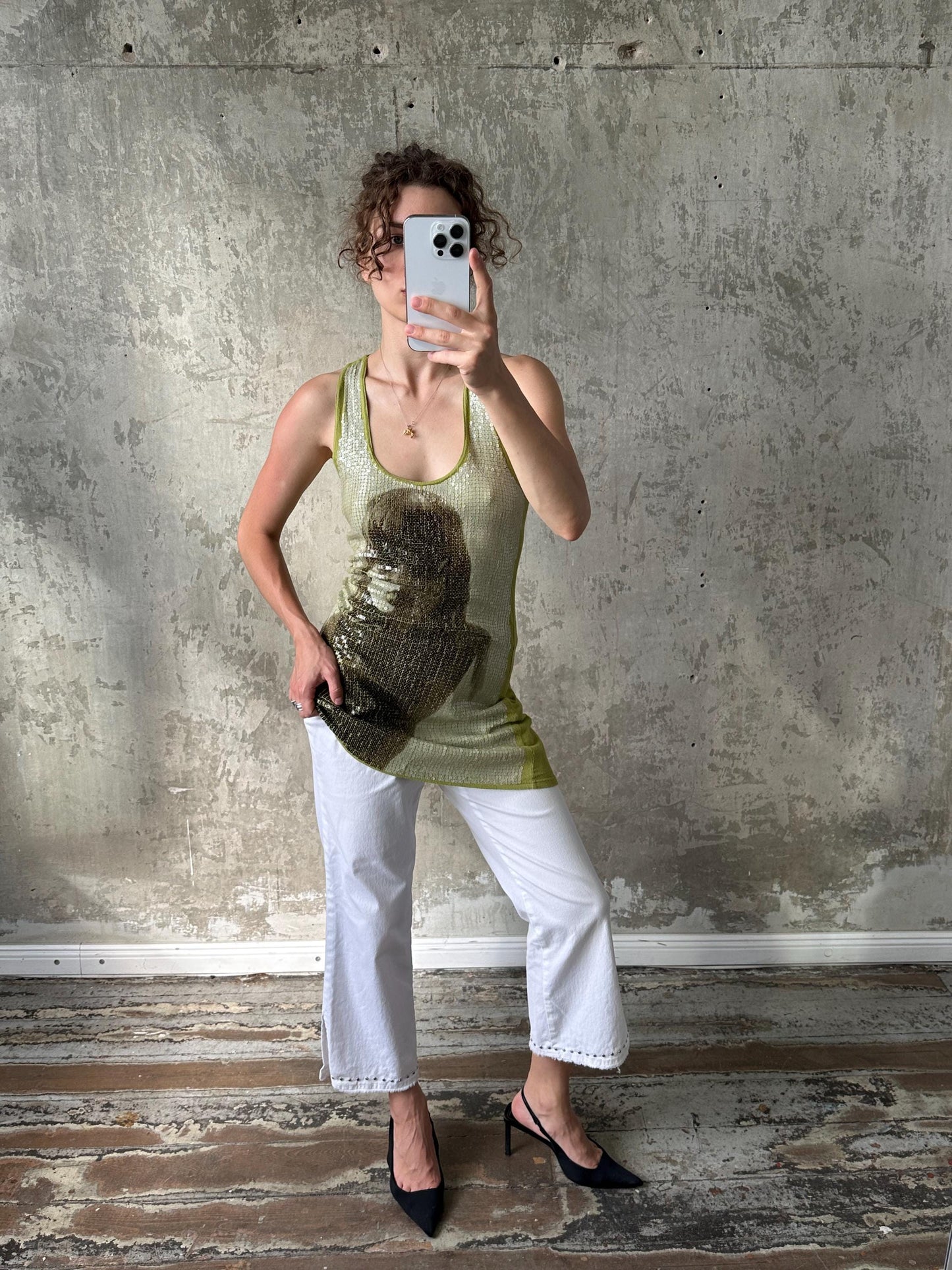 A woman is taking a selfie with a smartphone, standing in front of a concrete wall.