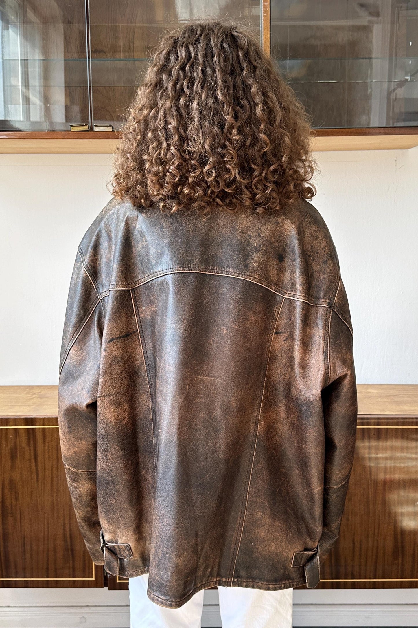 a person with curly hair wearing a brown leather jacket, facing away from the camera.