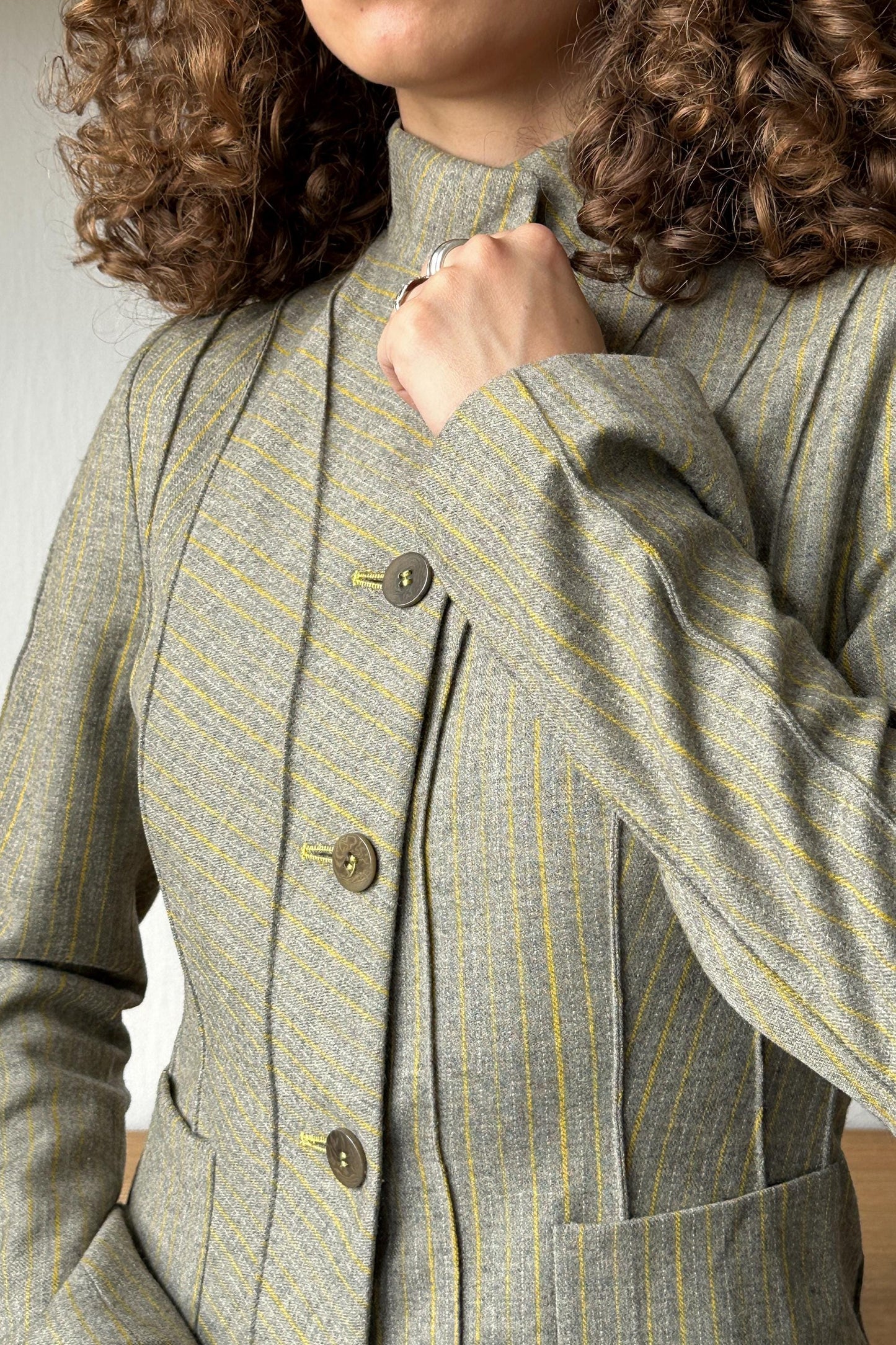 A close-up of a person wearing a gray and yellow striped jacket with a buttoned collar and sleeves.