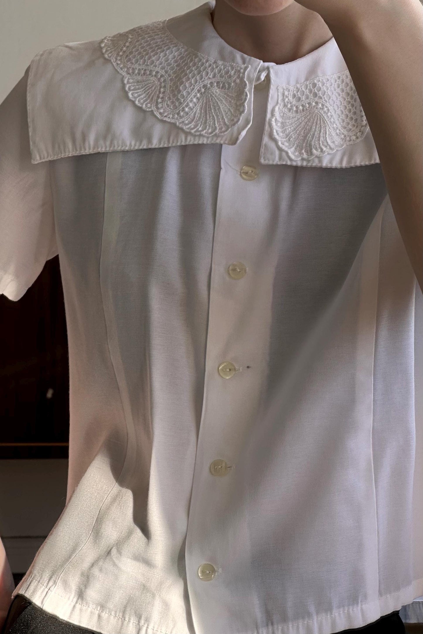 A close-up view of a person wearing a white collared shirt with a lace collar and buttons.