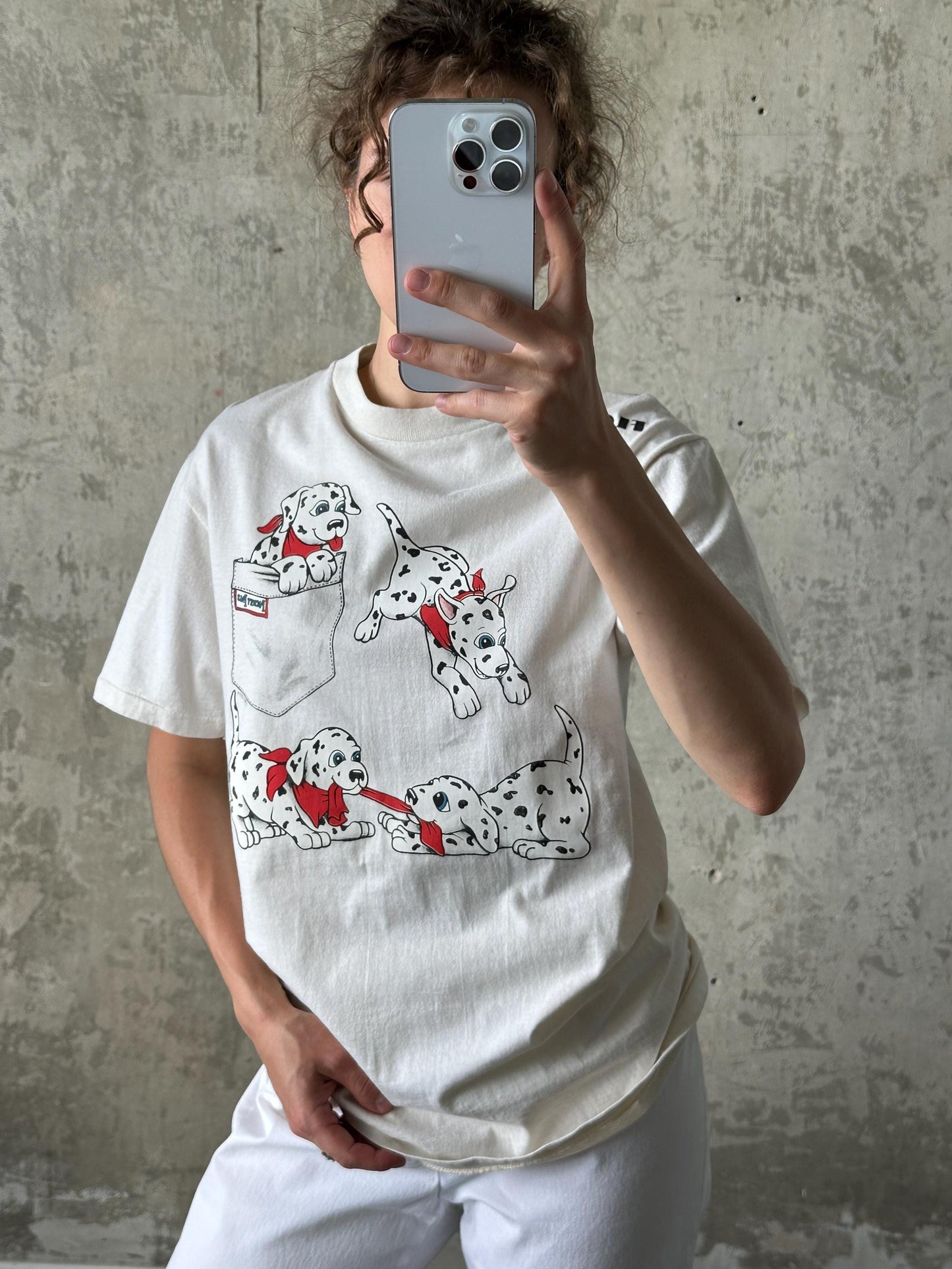 A person is taking a selfie with a smartphone, wearing a white t-shirt with a Dalmatian dog graphic printed on it.