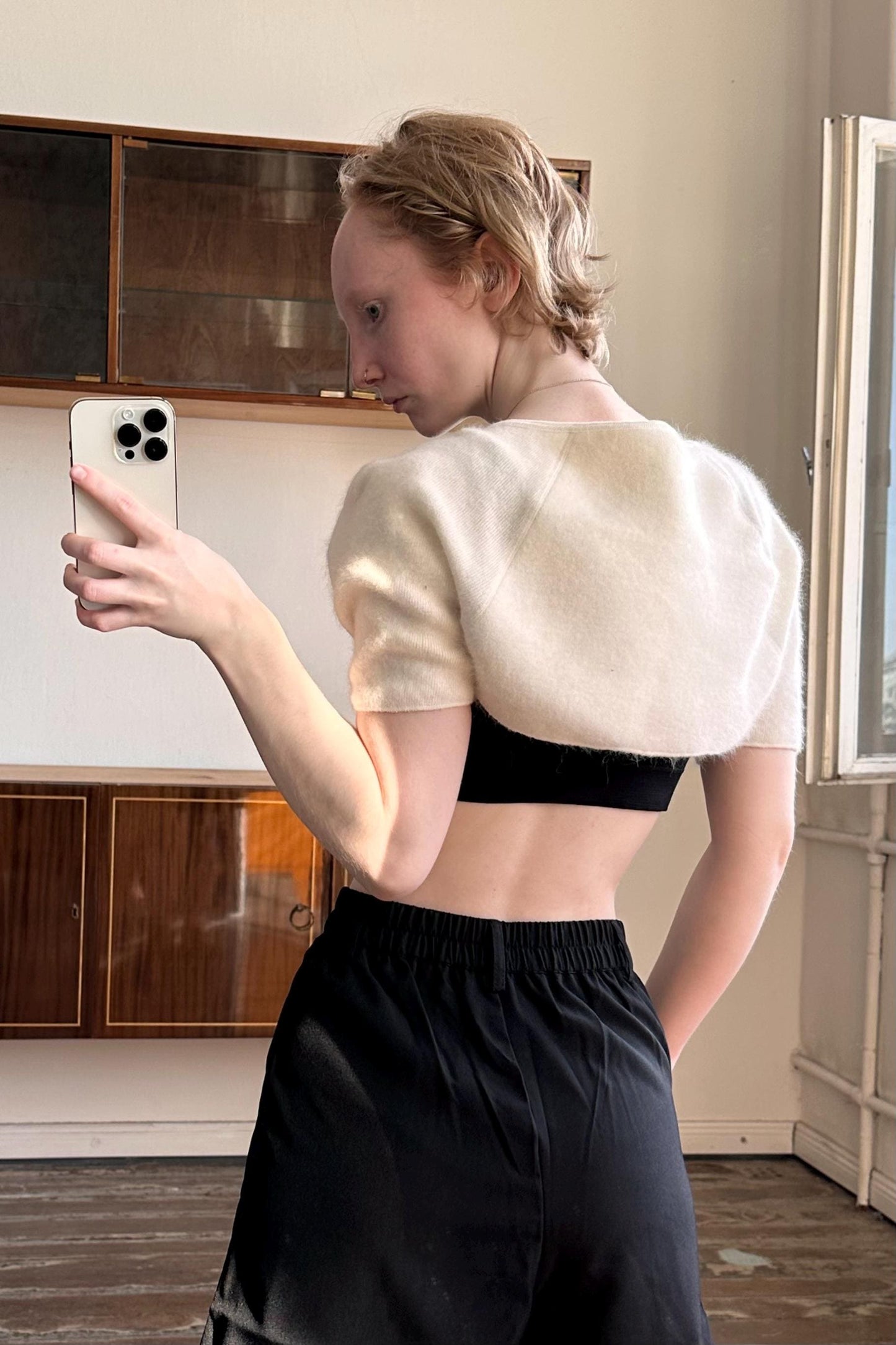 A woman is taking a selfie with a white phone in a room with wooden cabinets.