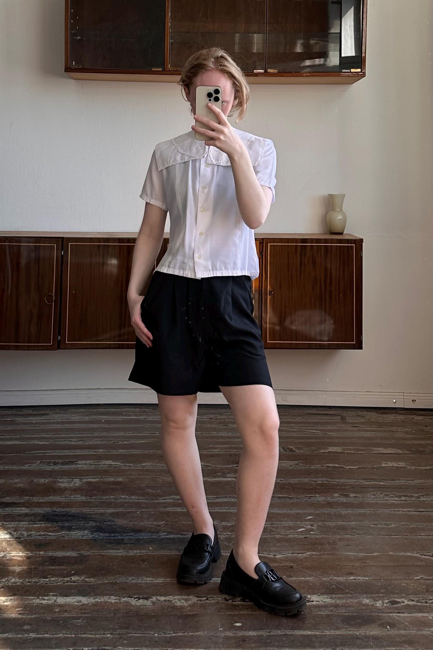 A person is taking a selfie in a room with wooden floors and a wooden cabinet.