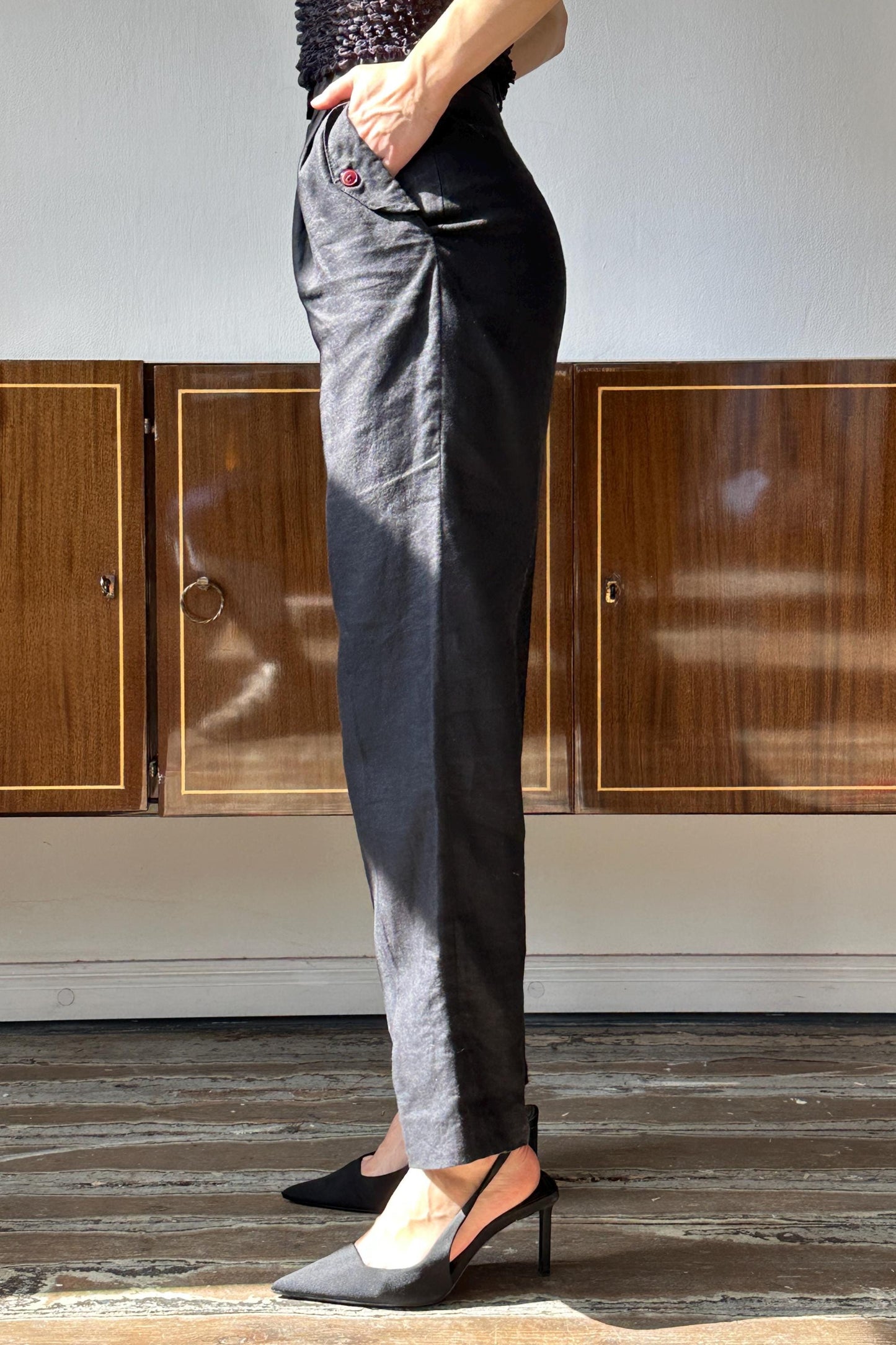 A person wearing black pants and high heels stands in front of wooden cabinets.