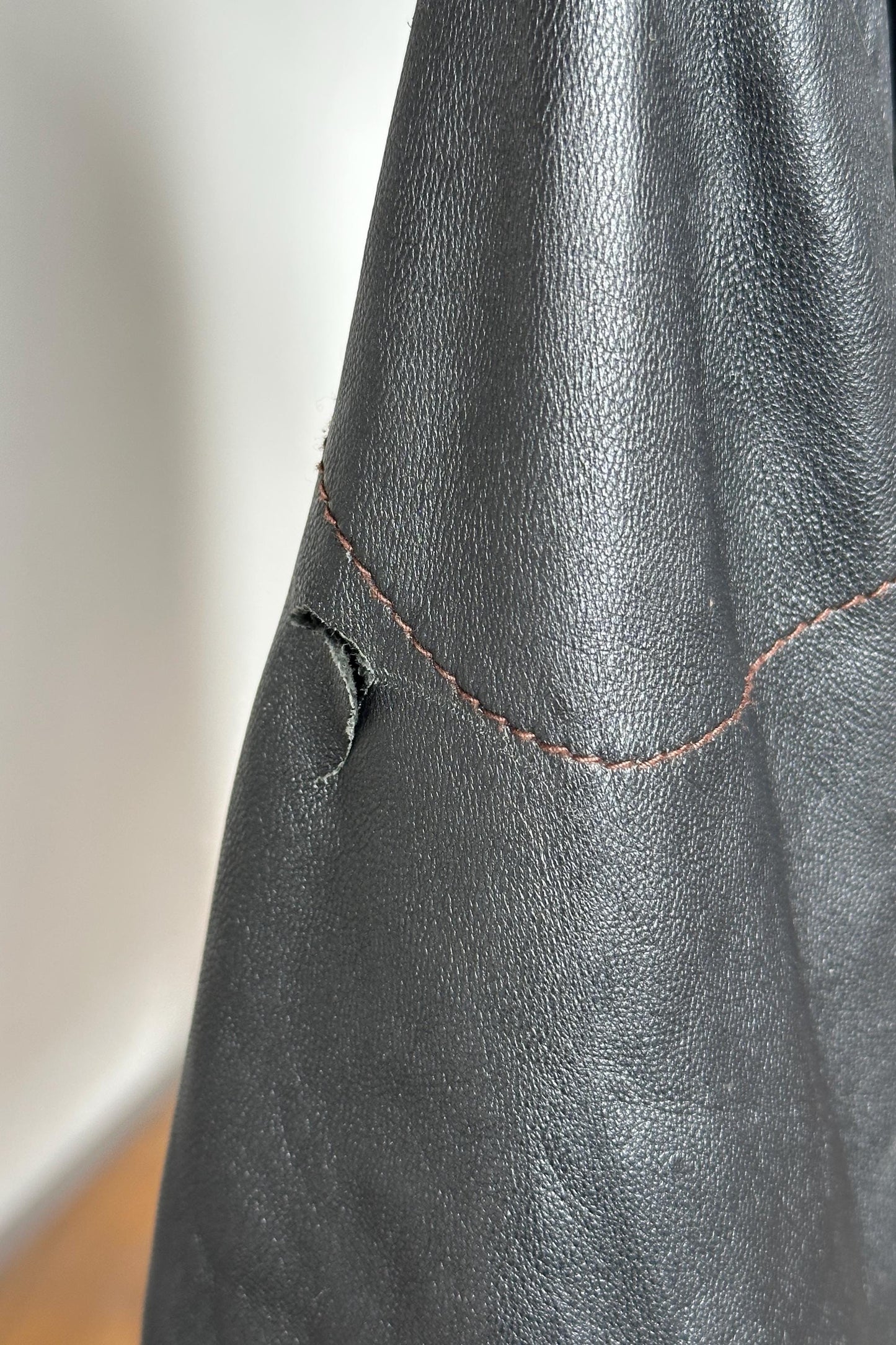 A close-up view of a black leather surface with a small tear or rip in the fabric.