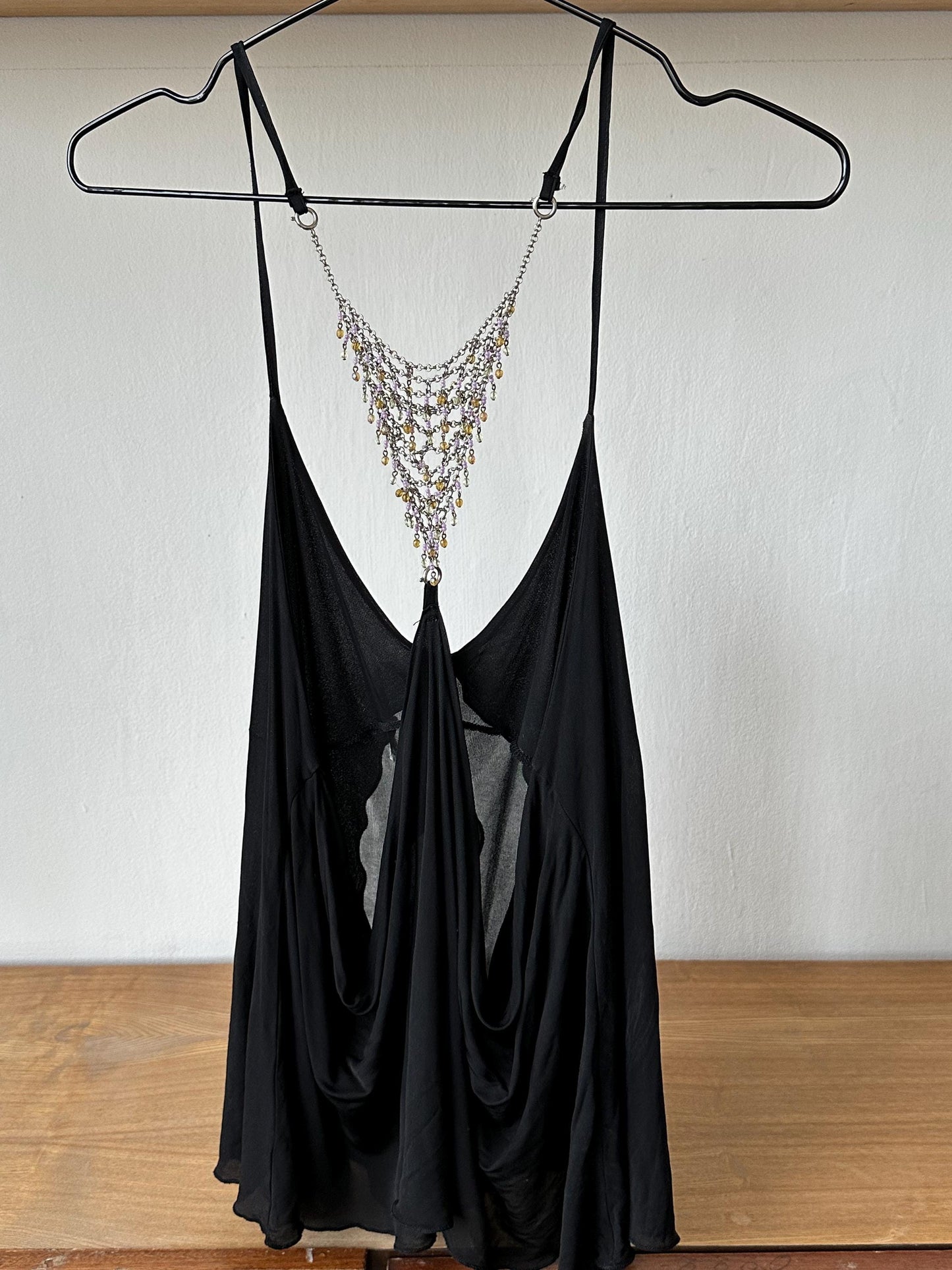 A black dress with a decorative necklace is hanging on a black hanger against a white wall.