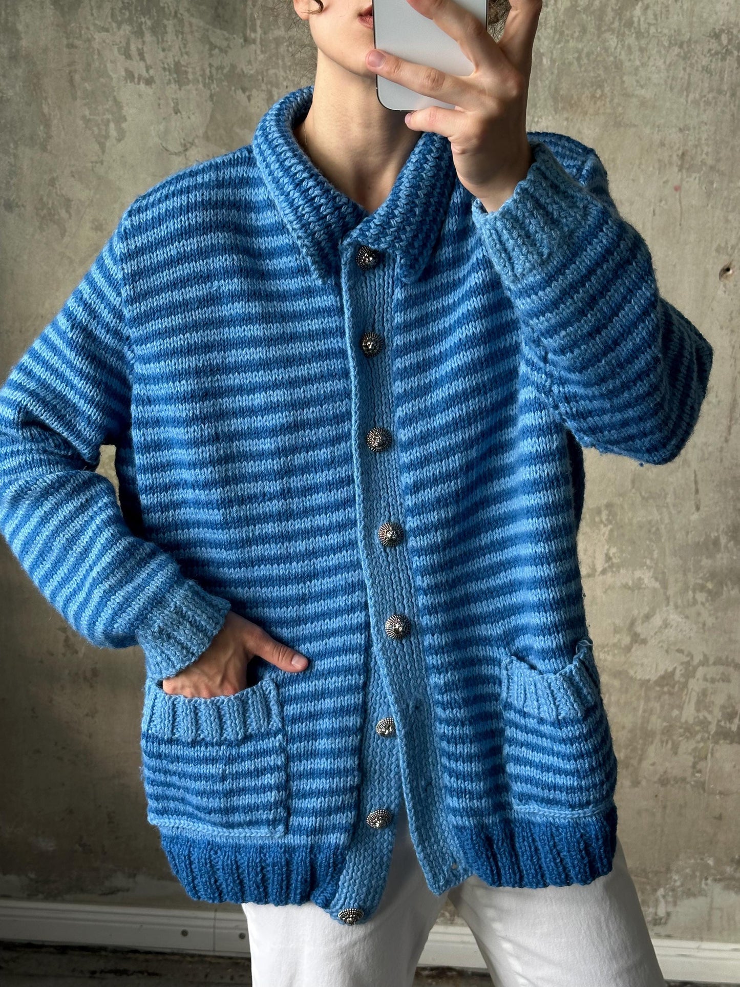 A person is taking a selfie with a blue and white striped cardigan, using a smartphone to capture the image.