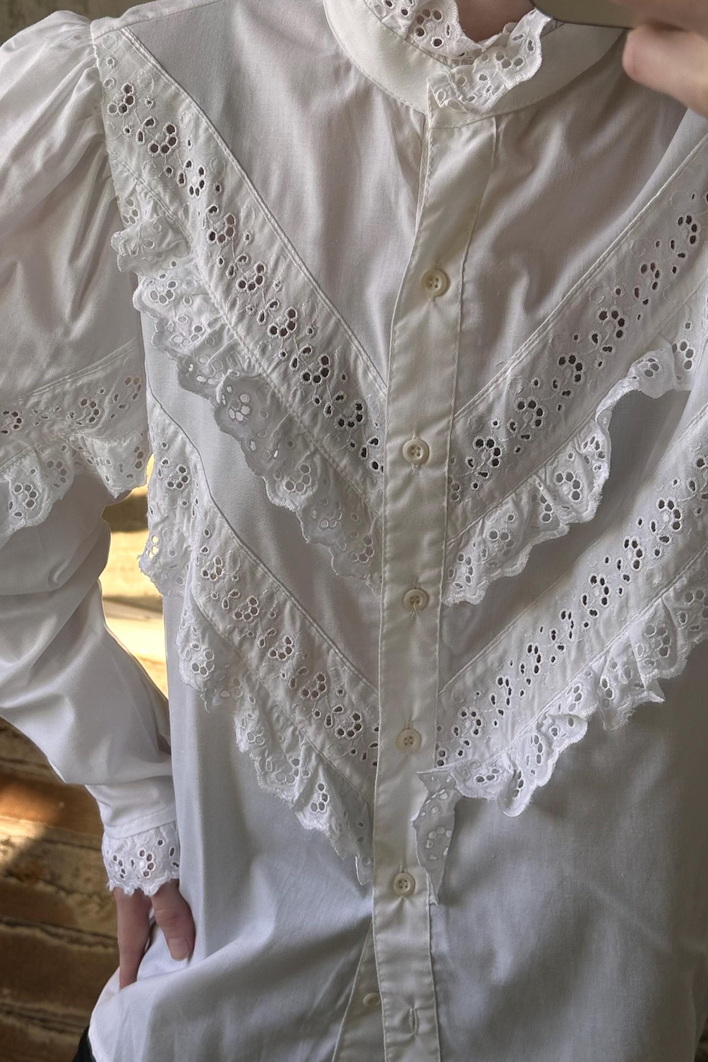 A close-up view of a white blouse with intricate lace detailing and buttons.