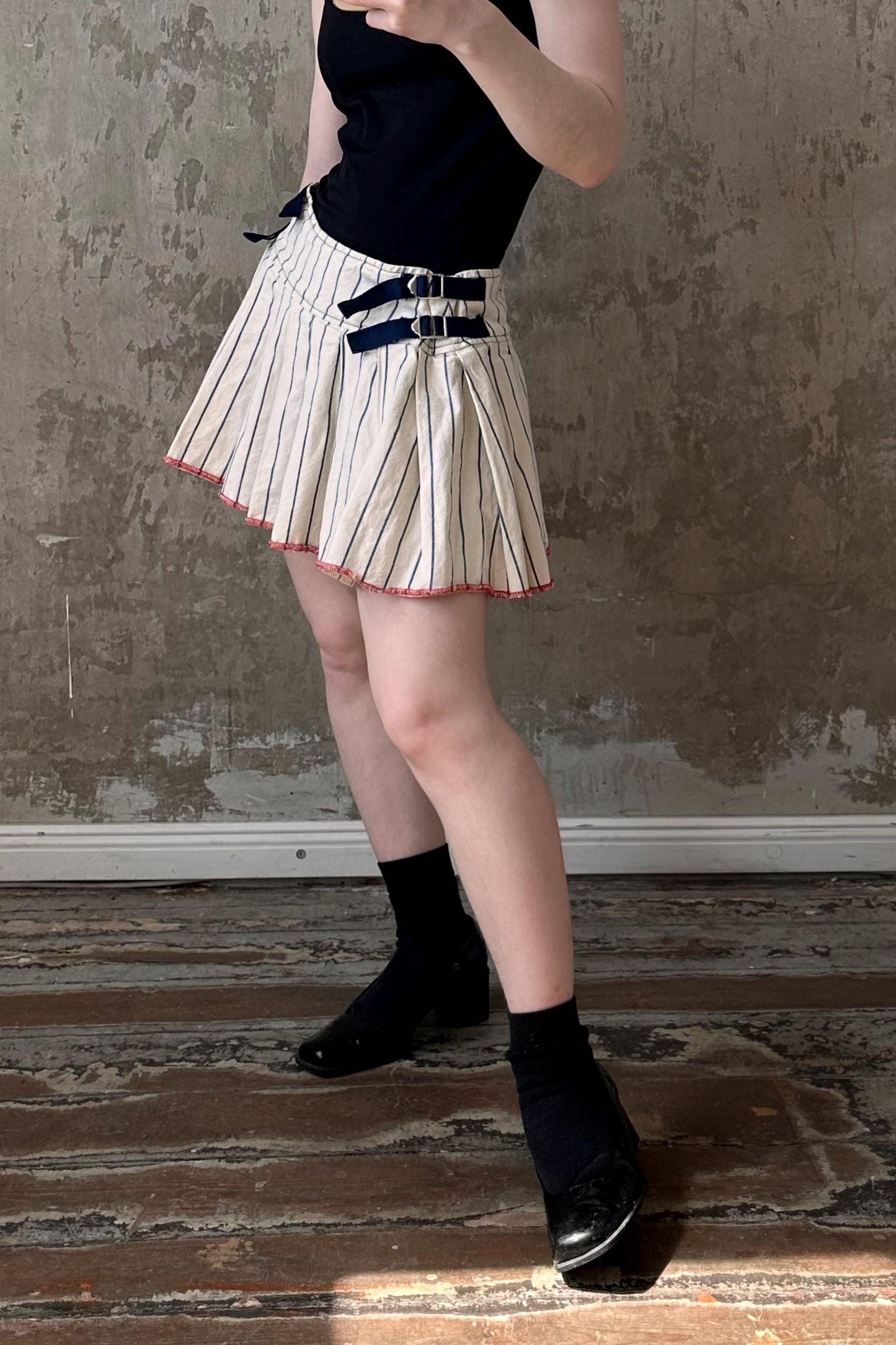 a woman in a skirt and hat taking a picture with her cell phone