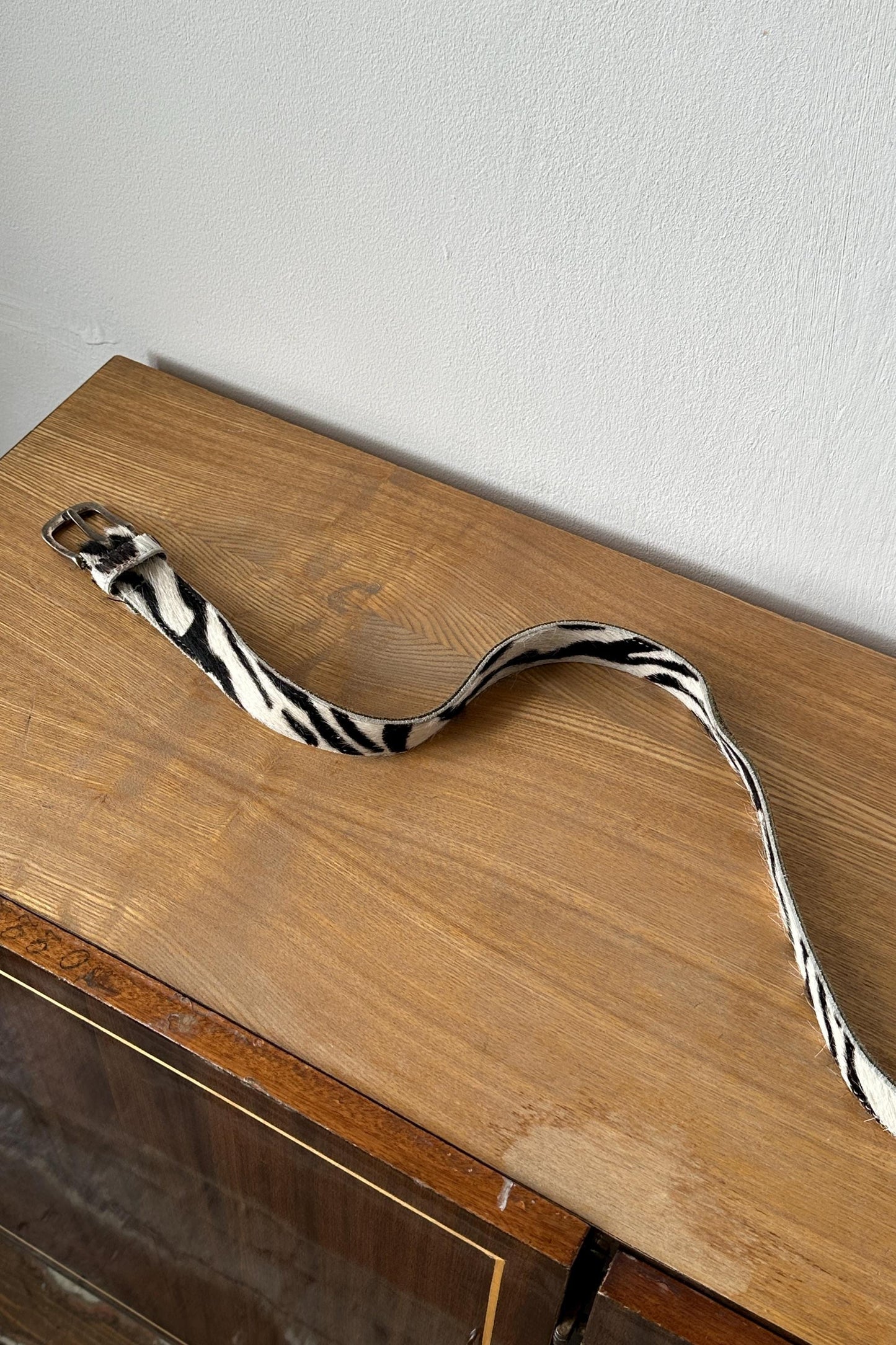 A zebra-striped belt is lying on a wooden surface against a white wall.