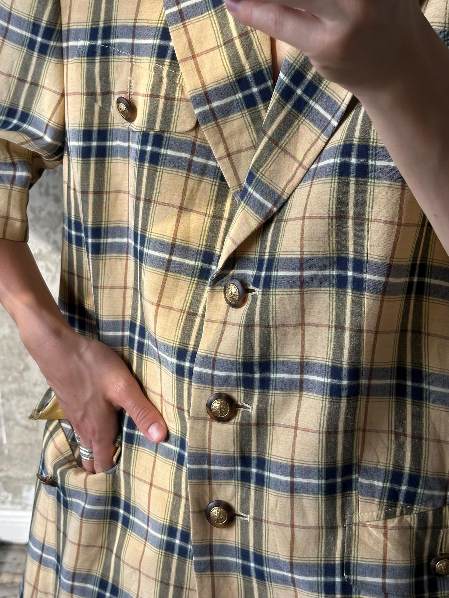 A close-up image of a person wearing a plaid jacket with buttons, showing the jacket's details and the person's hands.