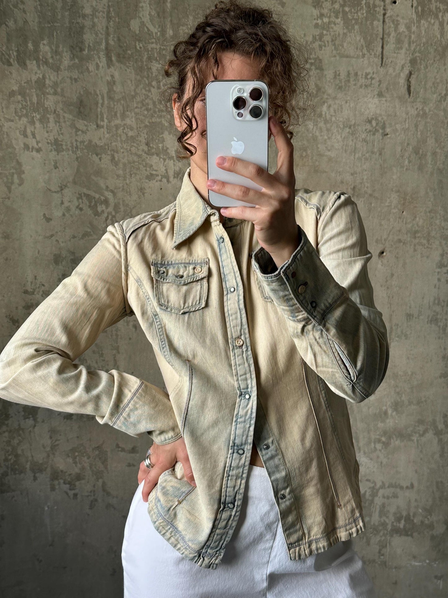 A person is taking a selfie with a smartphone, holding it up to their face against a concrete wall background.