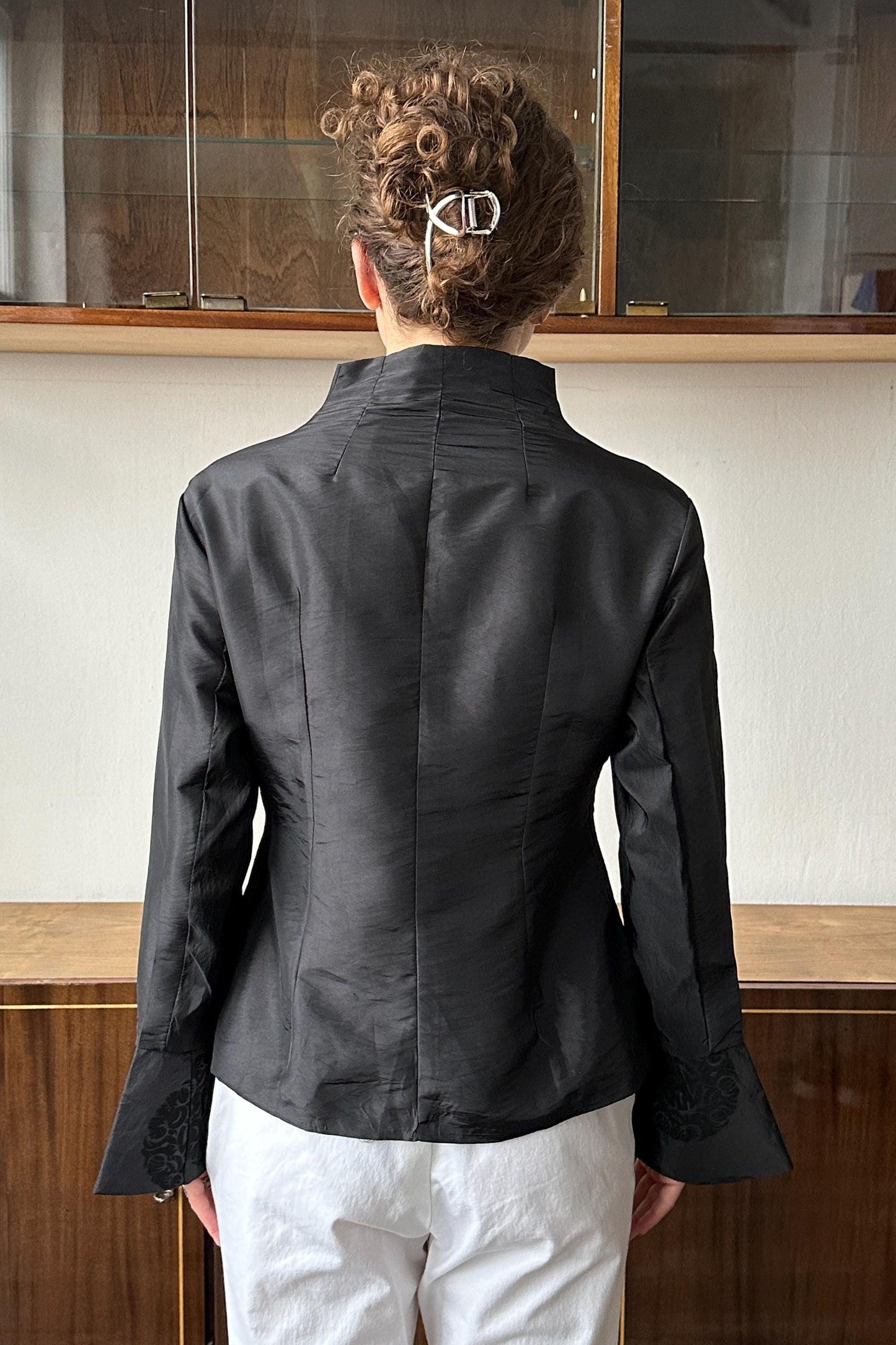 A person wearing a black blazer stands in front of a glass display case.