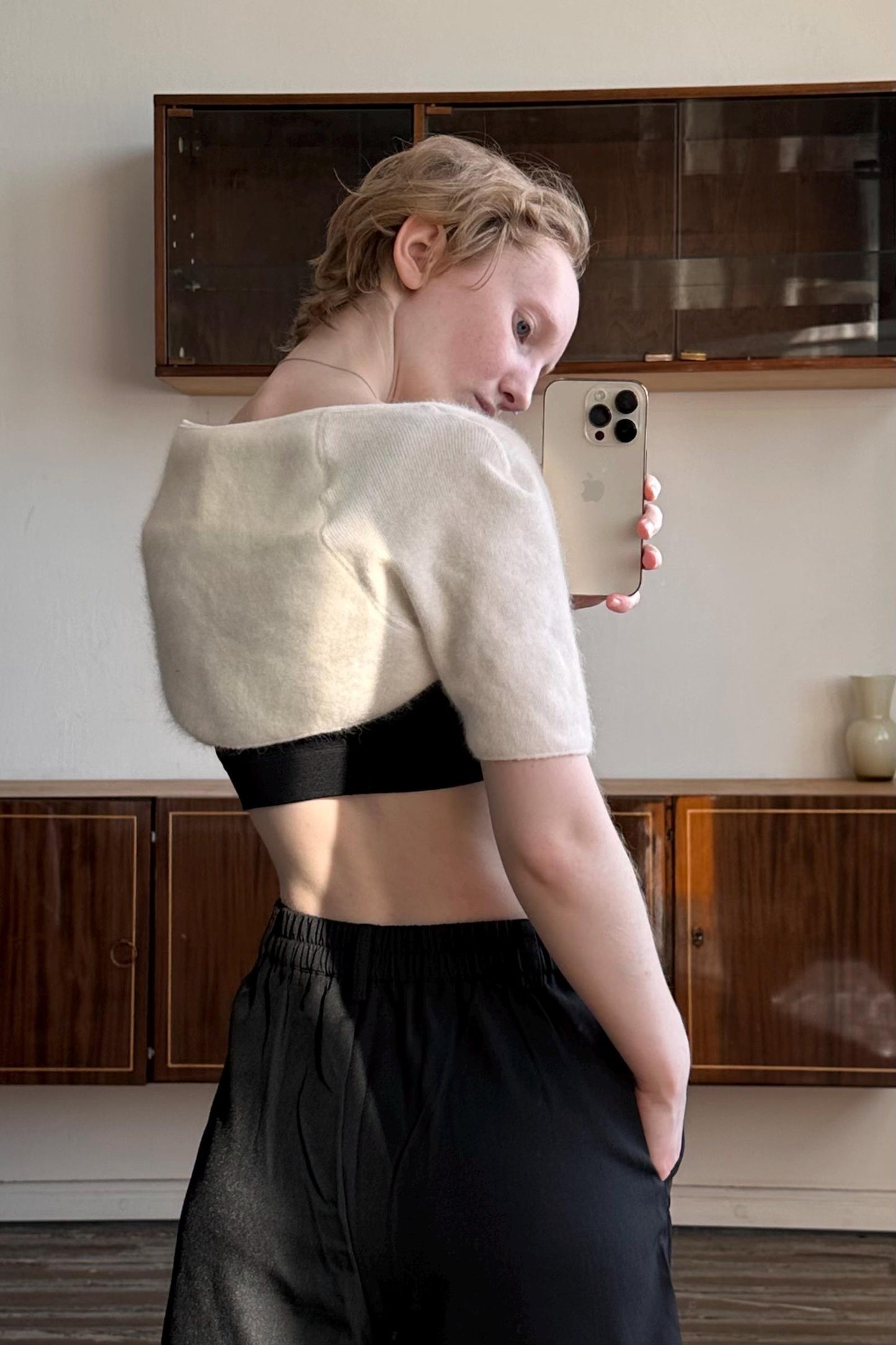A woman is taking a selfie with her iPhone in a room with wooden cabinets.