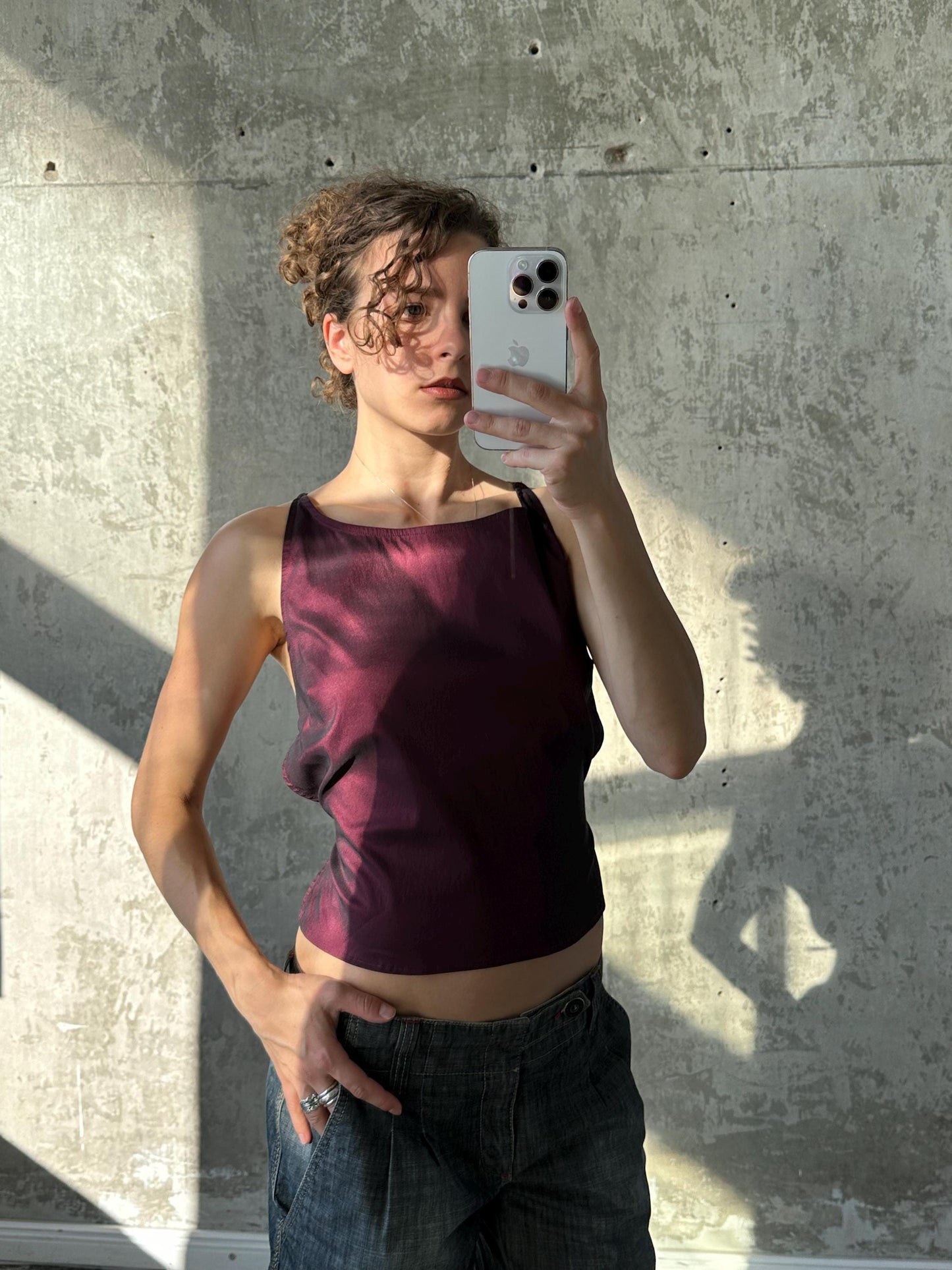 A person is taking a selfie with a smartphone, holding the device up to their face against a concrete wall.