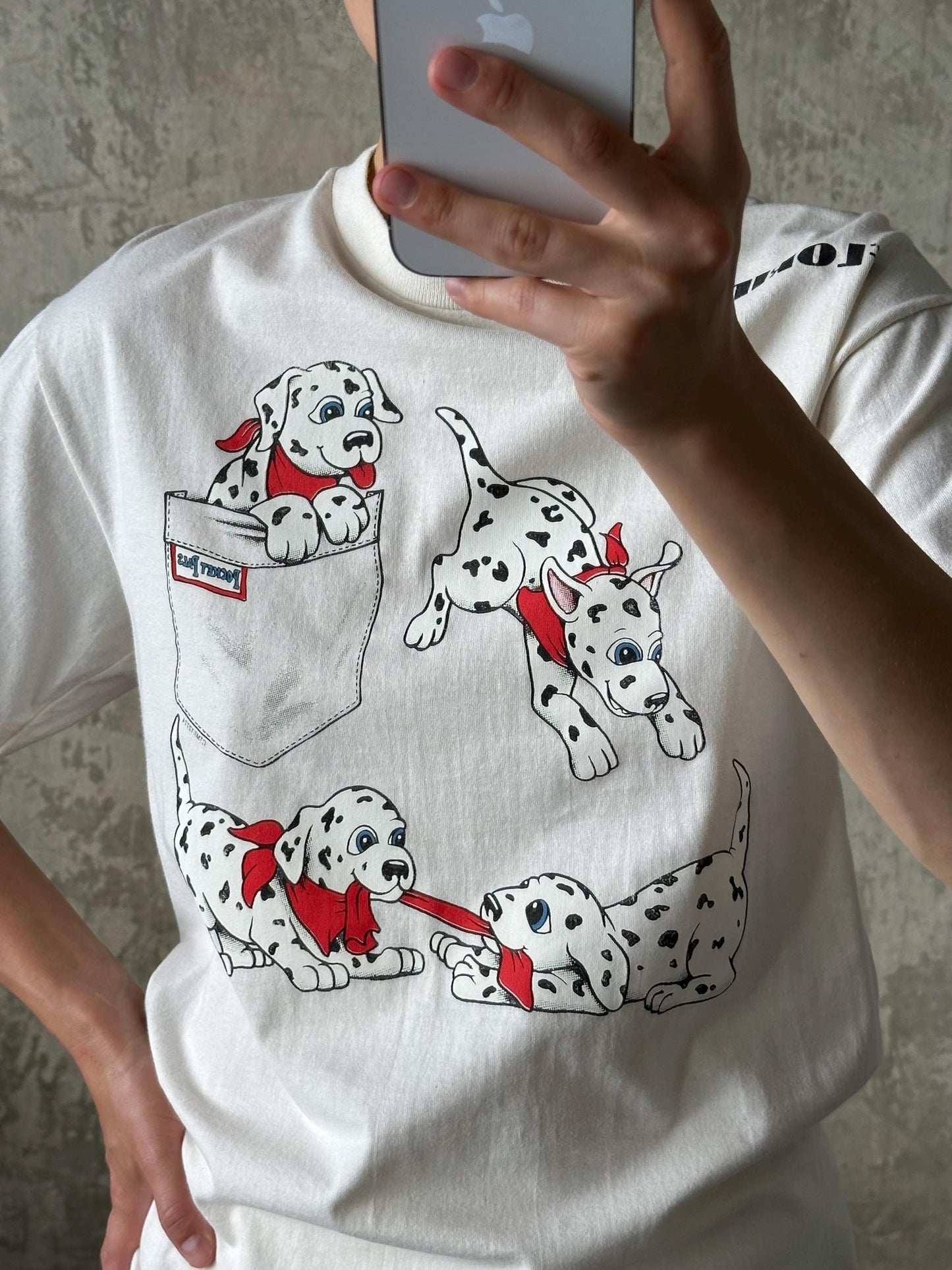 A person is taking a selfie with a white t-shirt featuring a graphic design of three Dalmatian dogs wearing red bandanas.