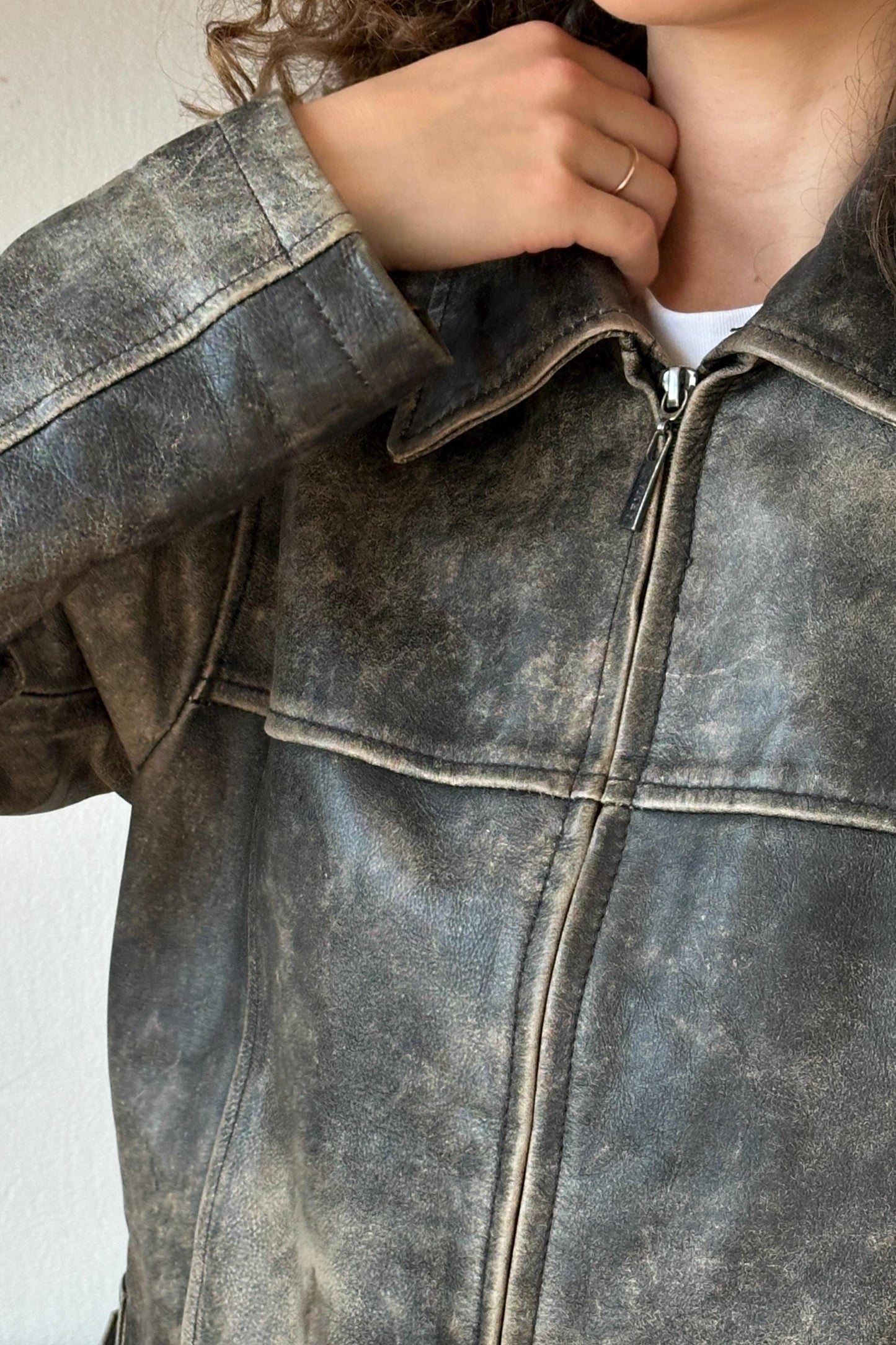 A close-up view of a person's hand adjusting the collar of a worn, gray leather jacket.