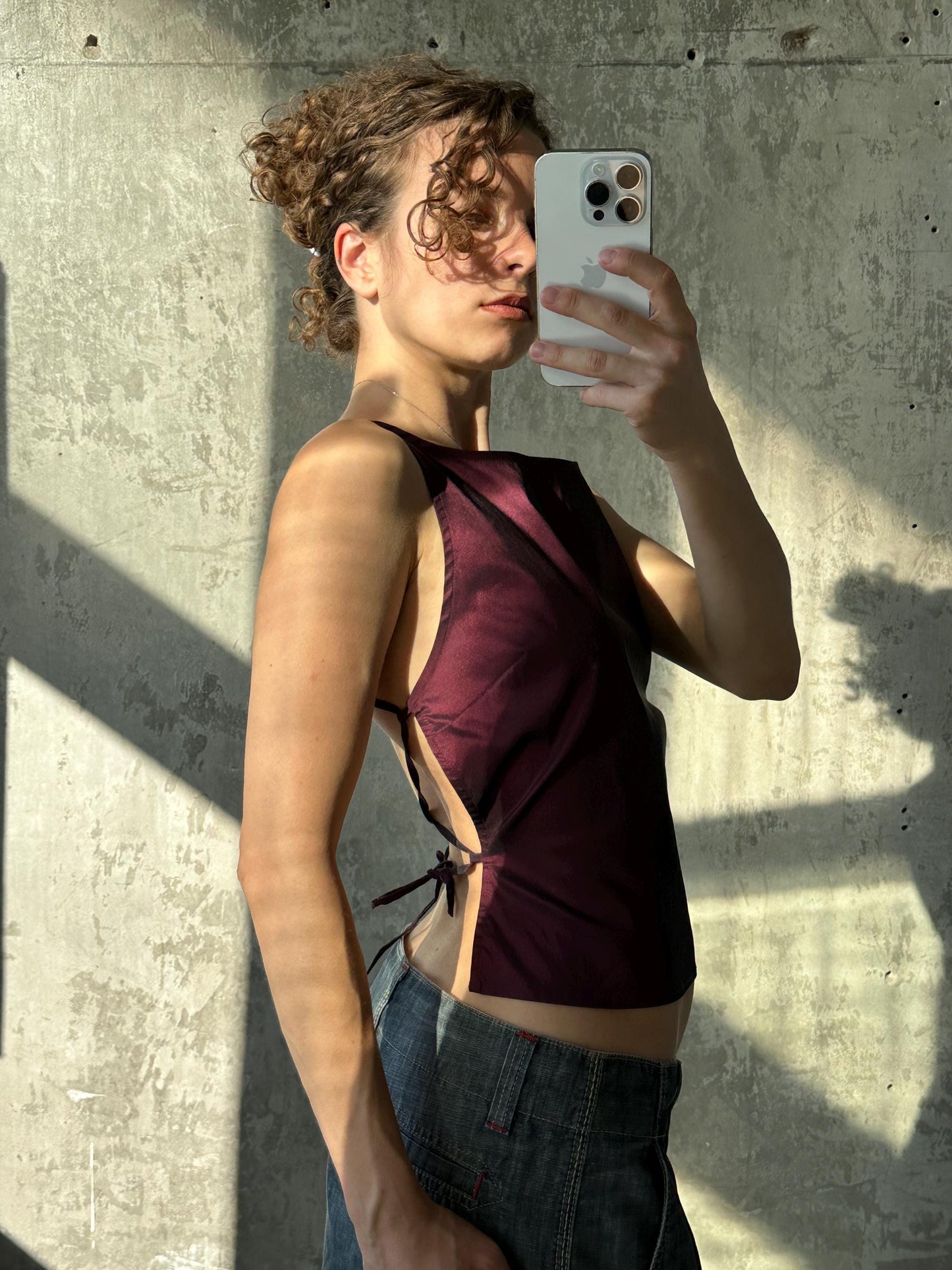 A woman is taking a selfie with her iPhone, holding the device up to her face against a concrete wall.
