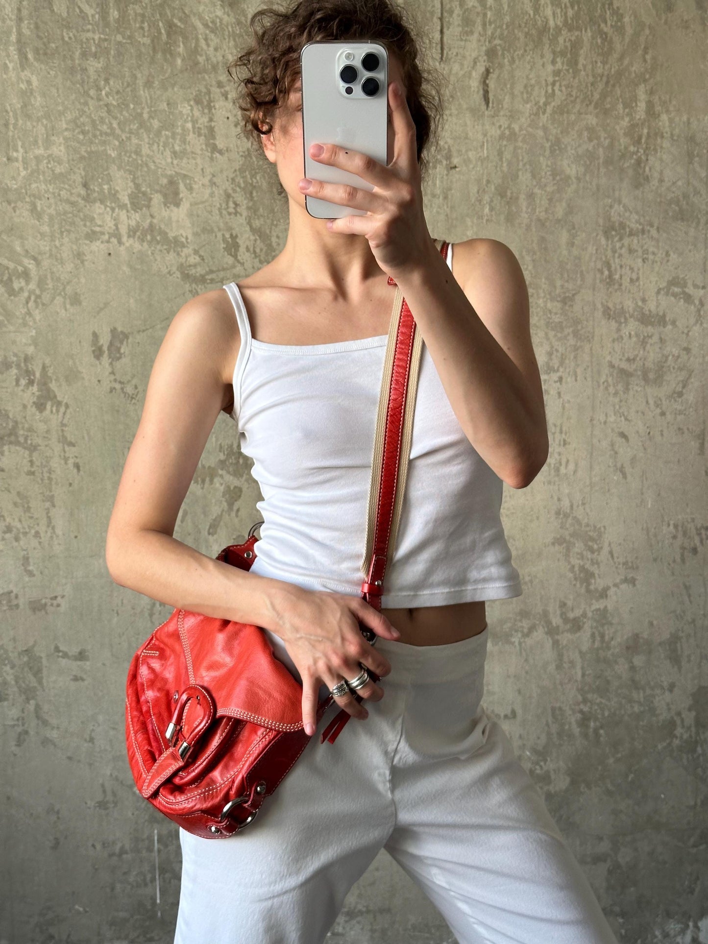 A person is taking a selfie with a red handbag in front of a concrete wall.