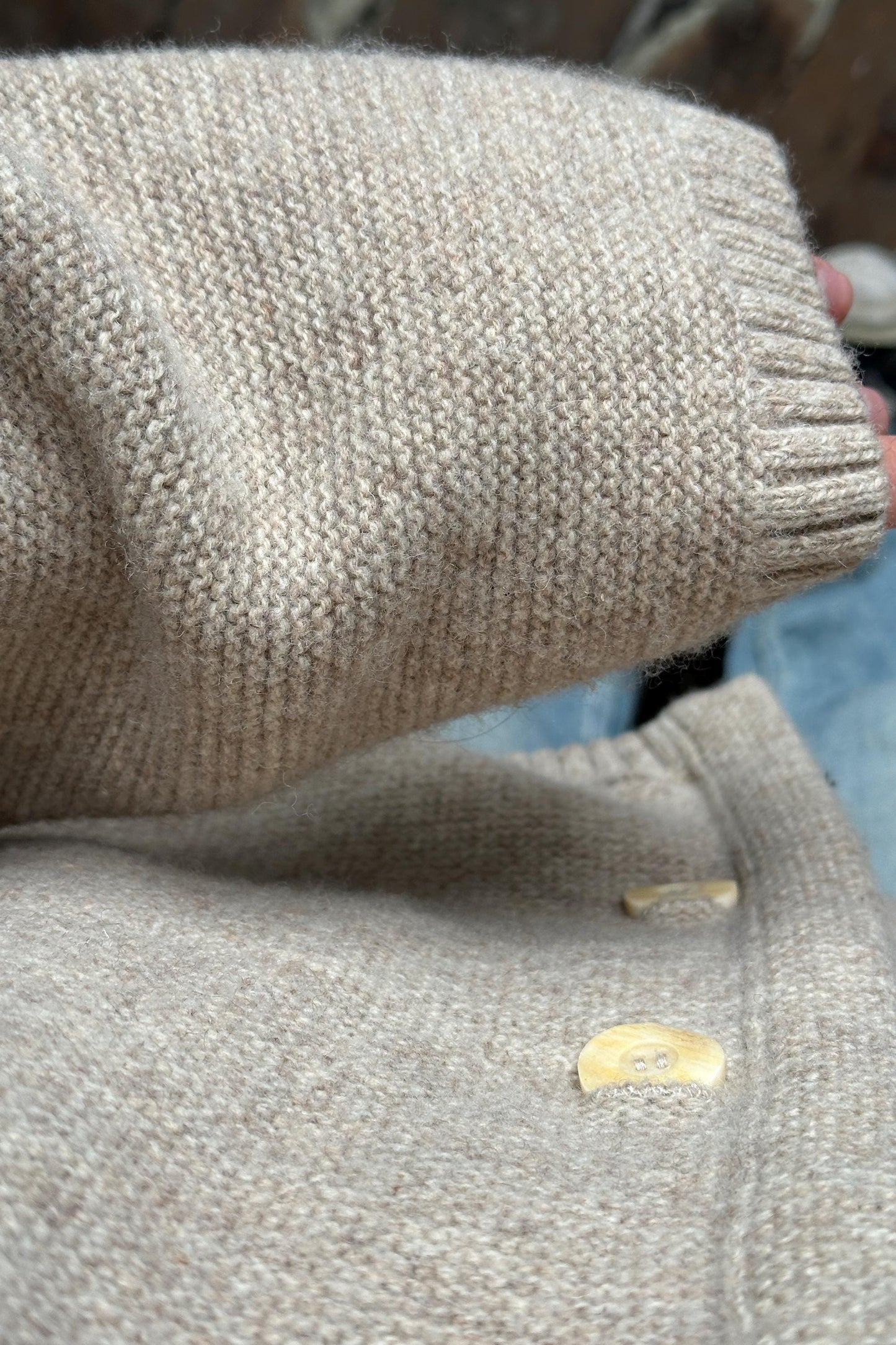 A close-up view of a beige knitted sweater with a button on the sleeve.