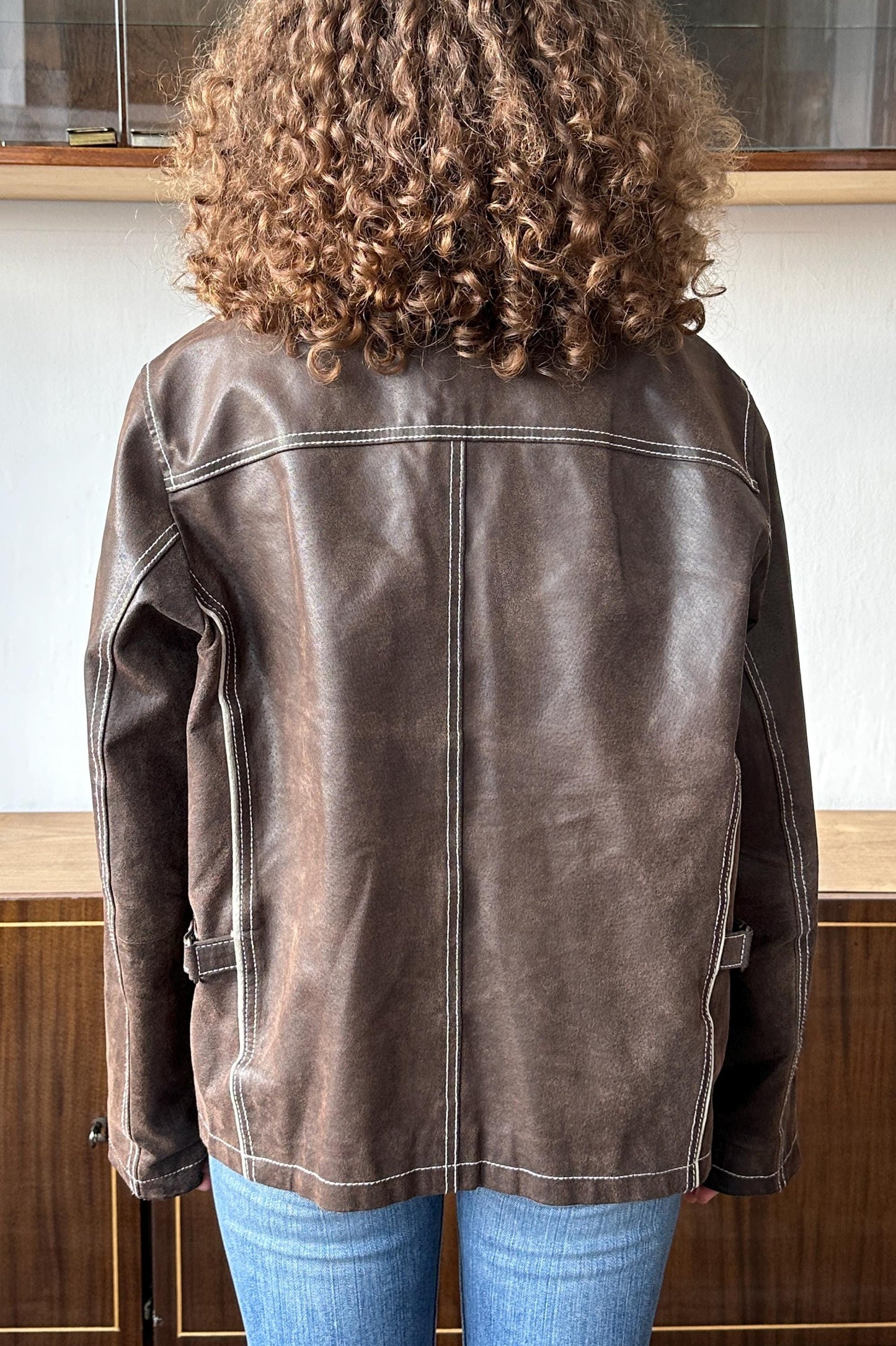 the back of a person wearing a brown leather jacket with a distinctive zipper detail.