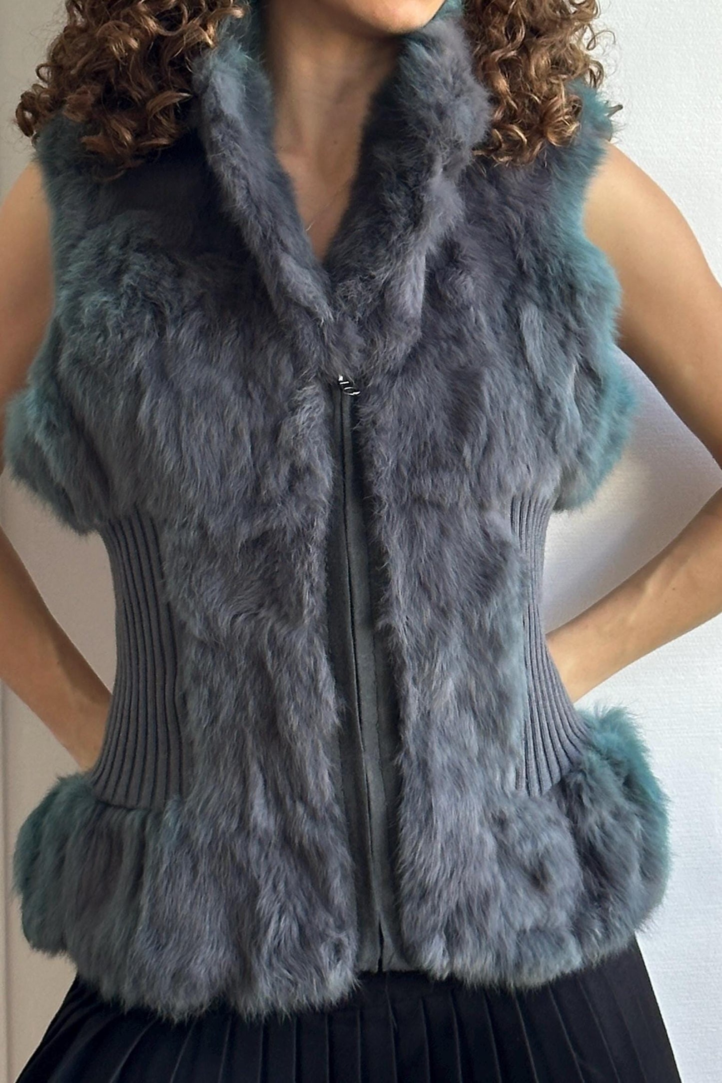 A close-up image of a person wearing a gray fur vest with a zipper and fur trim.